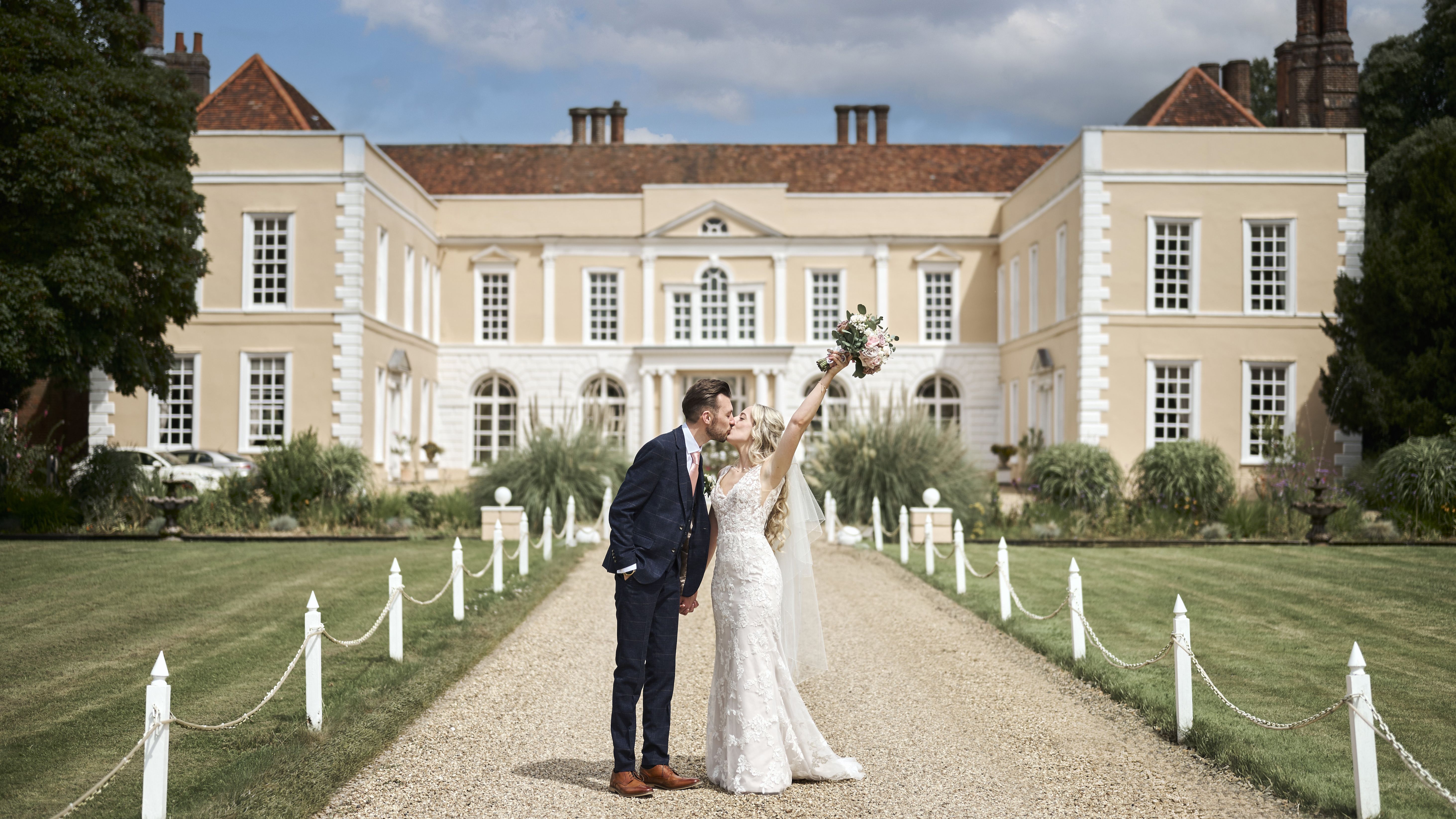 Bride and groom kissing outside Hintlesham Hall on a sunny day.