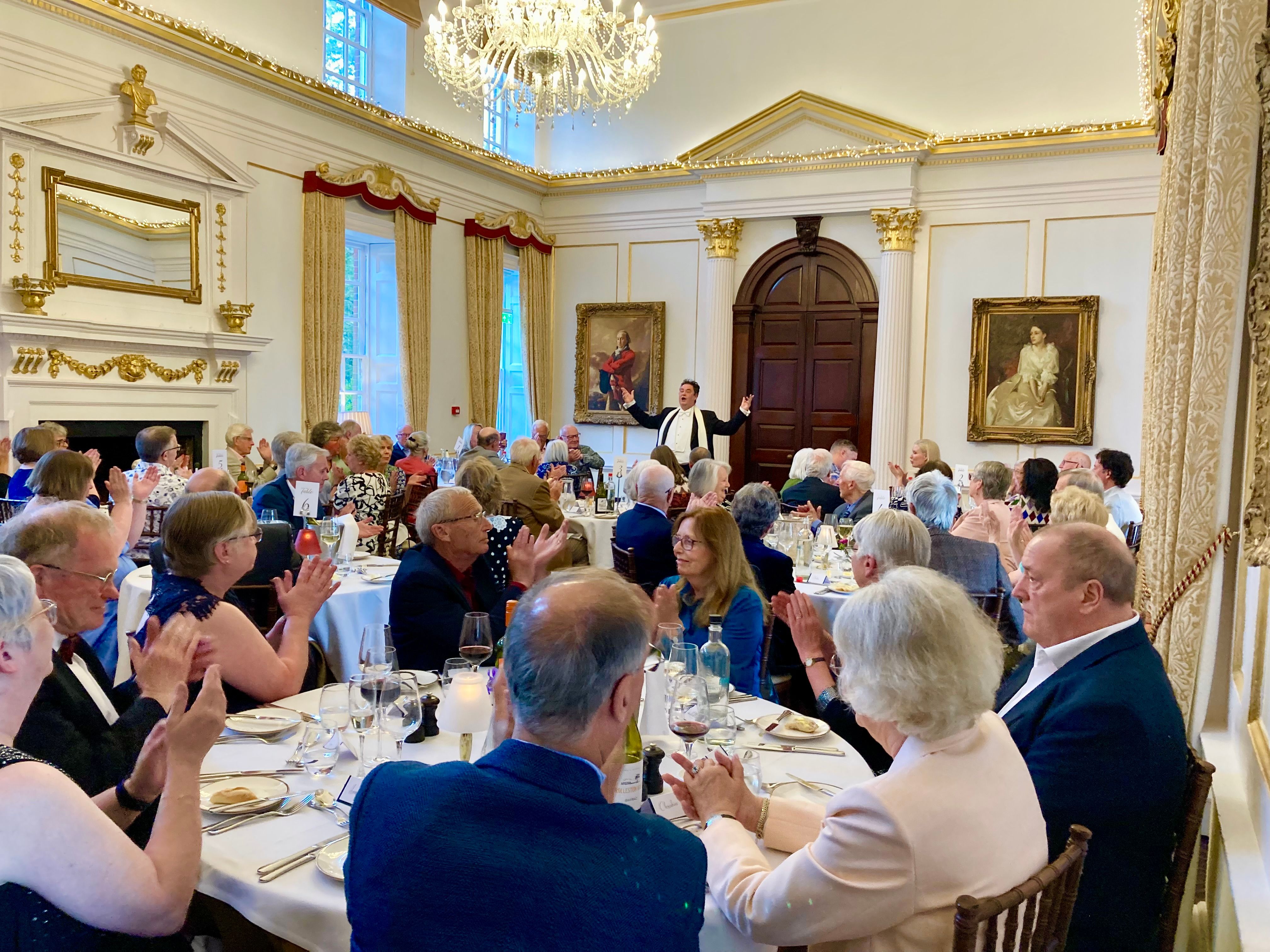Elegant dinner event with guests applauding a performer in a grand, ornately decorated room