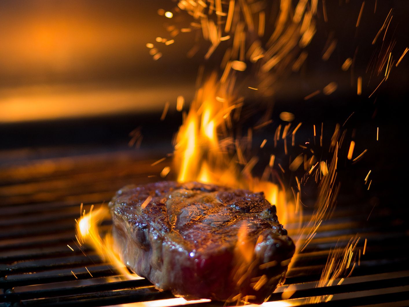 Steak searing on a barbecue grill with flames and flying sparks