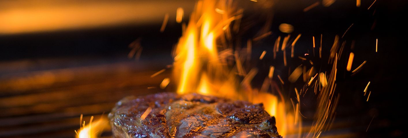 Steak searing on a barbecue grill with flames and flying sparks