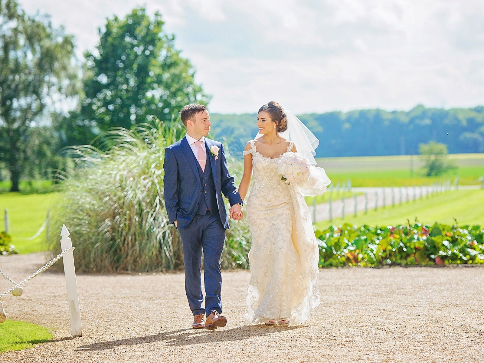 Bride and groom walking hand in hand along a countryside path on their wedding day