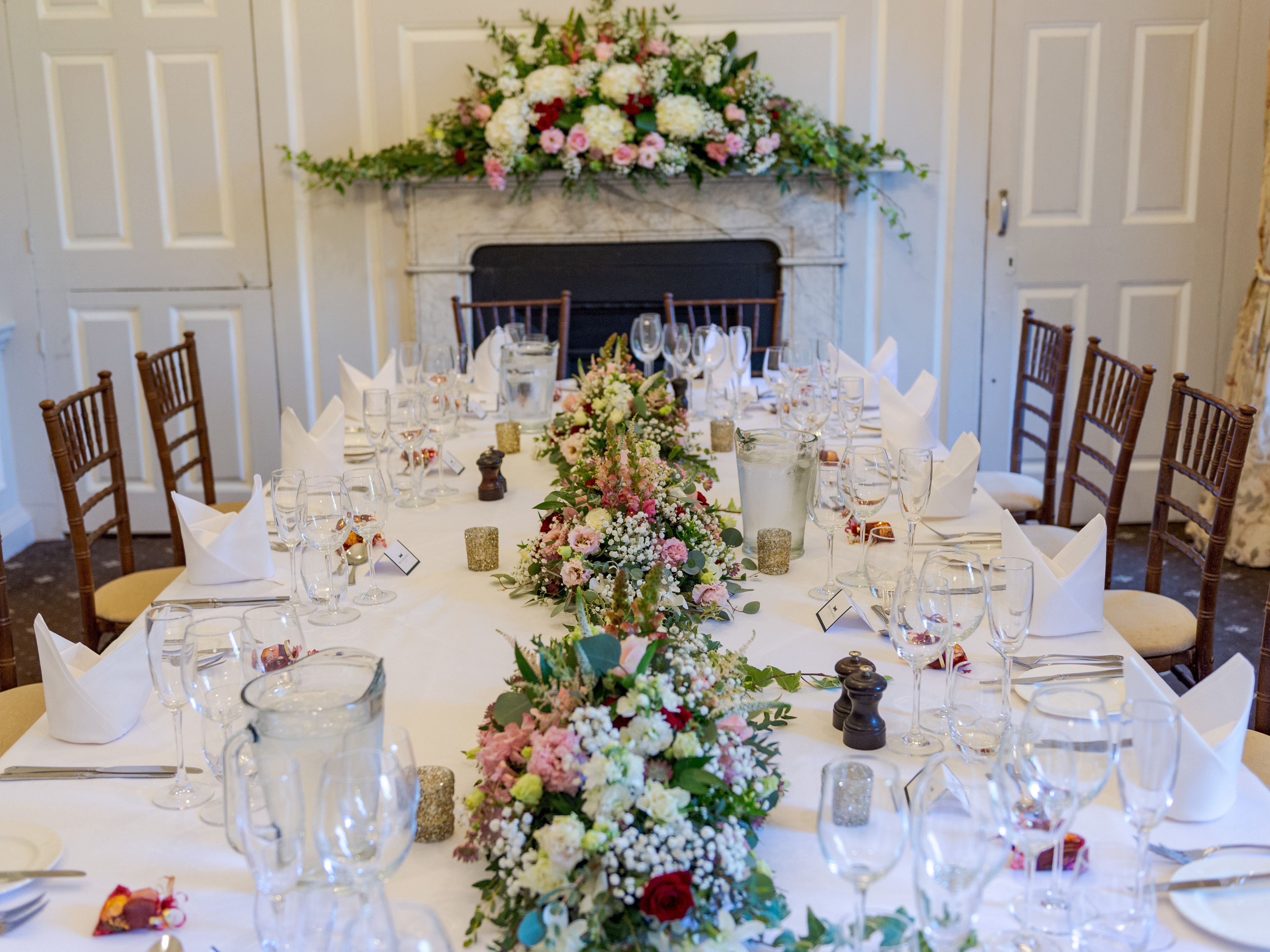 Elegant banquet table set with white linen, folded napkins and floral centrepieces in a formal dining room