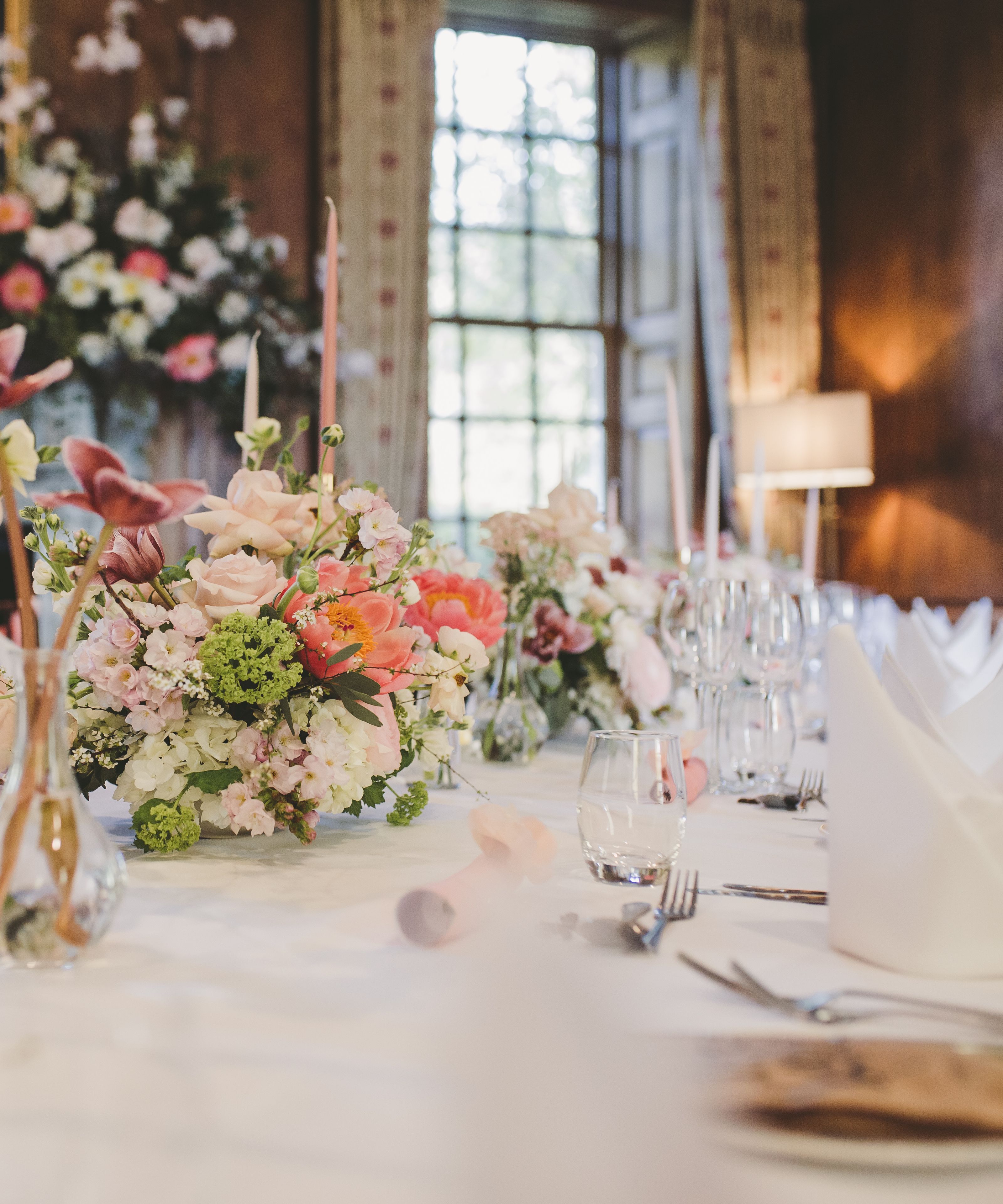 Elegant dining table set in a wood-panelled parlour with pastel floral centrepieces and tall pink candles