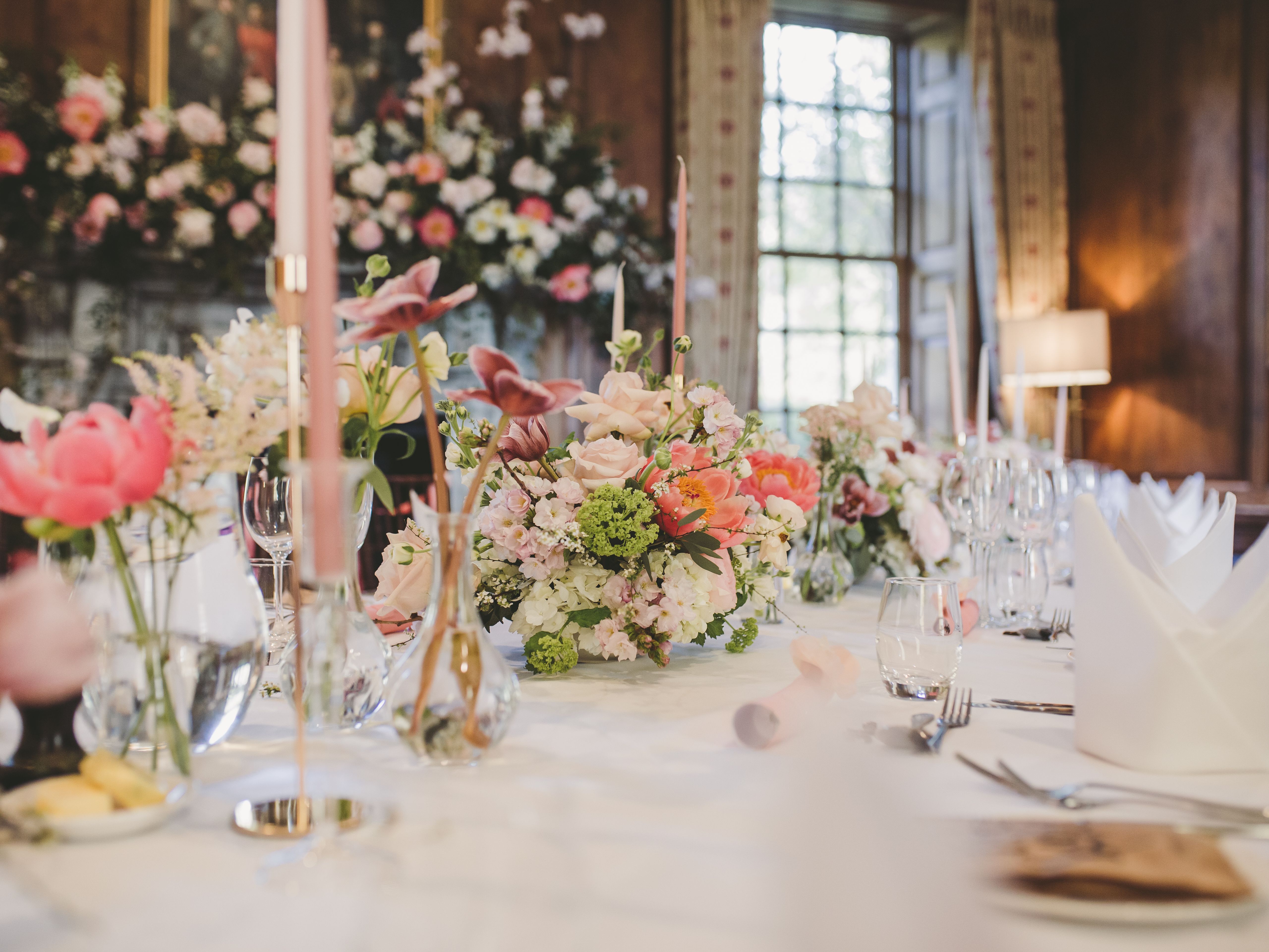 Elegant dining table set in a wood-panelled parlour with pastel floral centrepieces and tall pink candles
