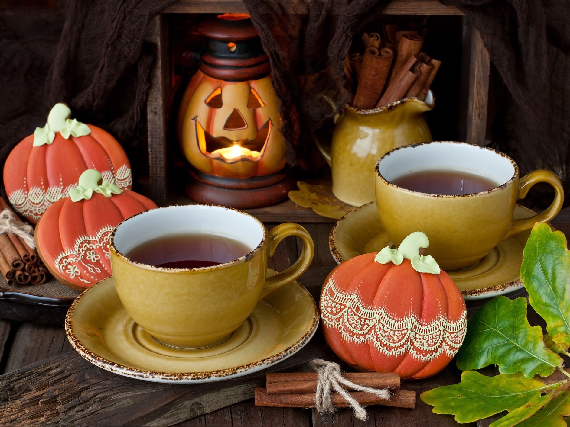 Autumn still life with two cups of tea, decorative pumpkins, cinnamon sticks and a glowing jack-o'-lantern