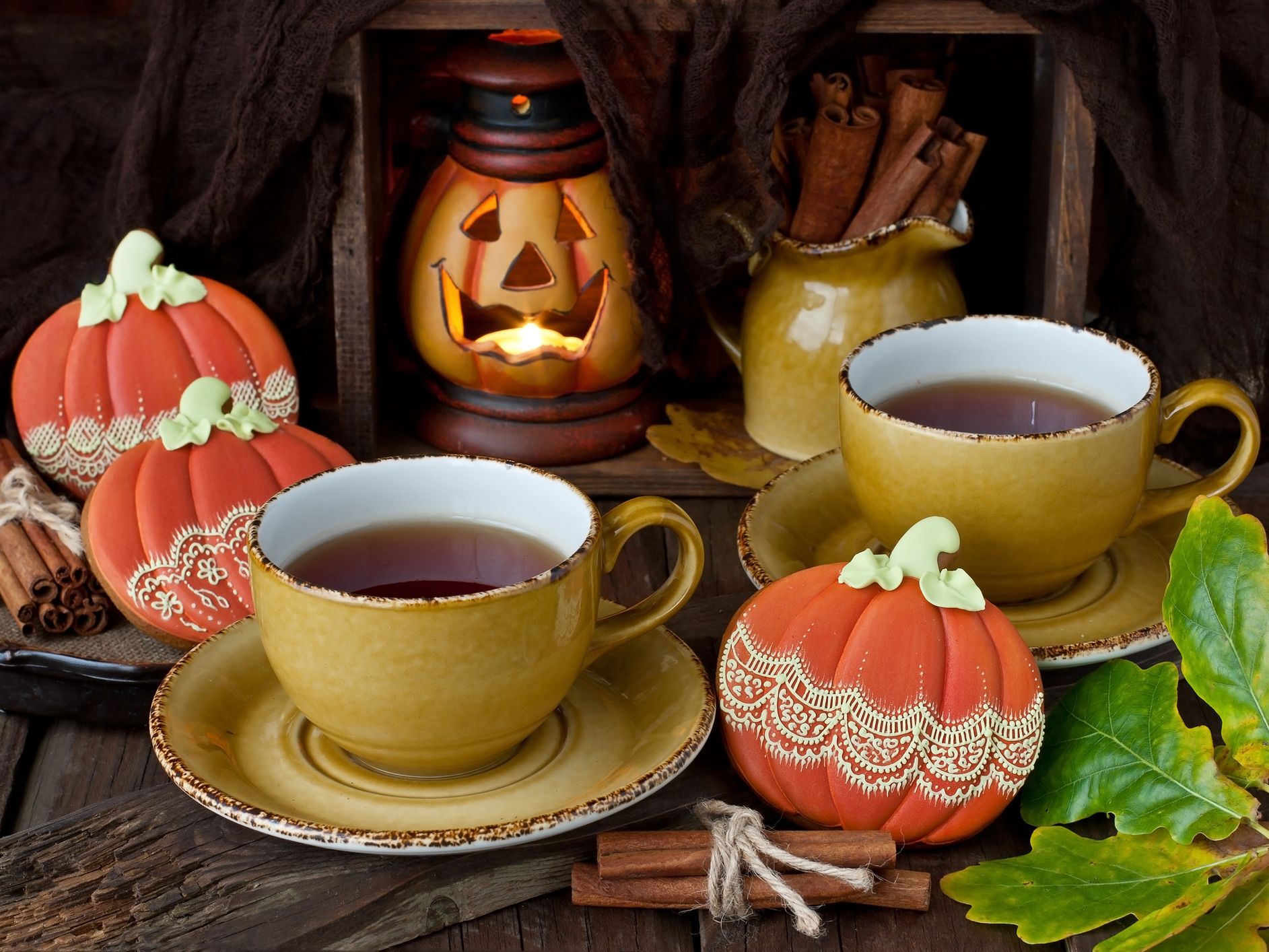Autumn still life with two cups of tea, decorative pumpkins, cinnamon sticks and a glowing jack-o'-lantern