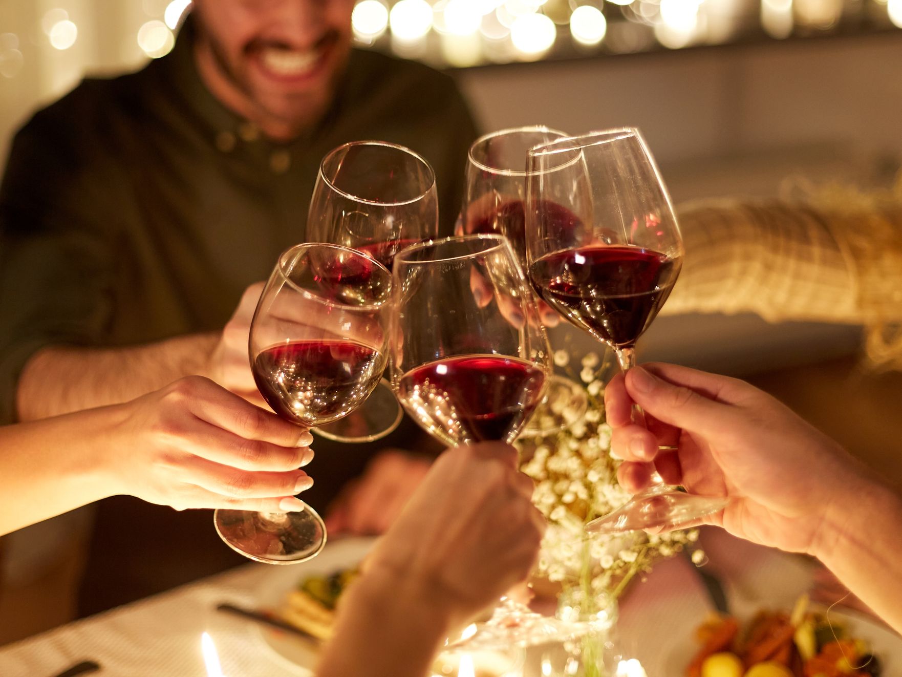 Friends clinking glasses of red wine at a candlelit dinner table