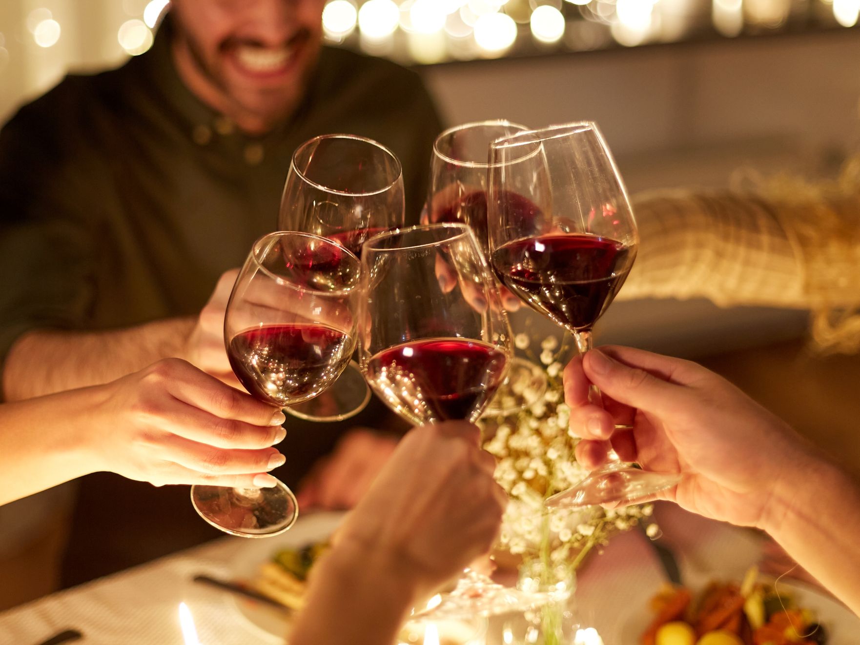 Friends clinking glasses of red wine at a candlelit dinner table