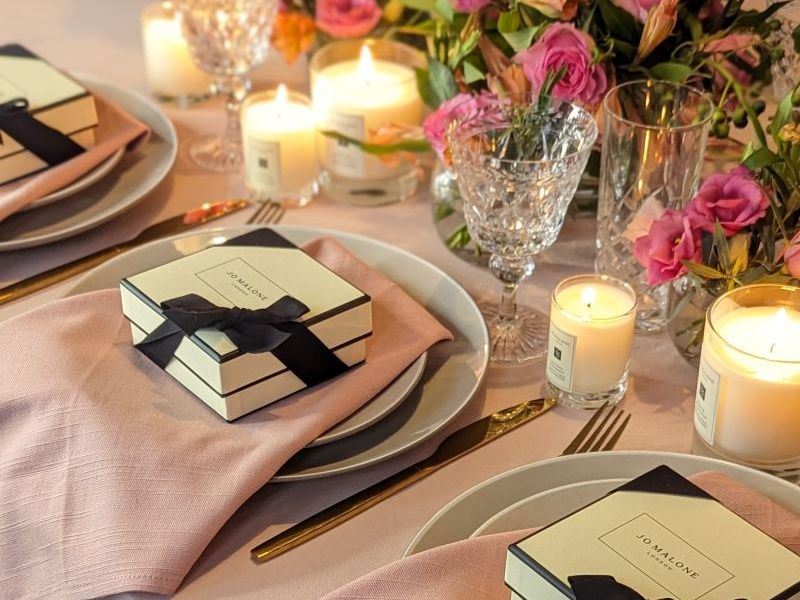 Elegant table setting with pink napkins, lit candles, crystal glasses and pink floral centrepieces, with gift boxes on plates