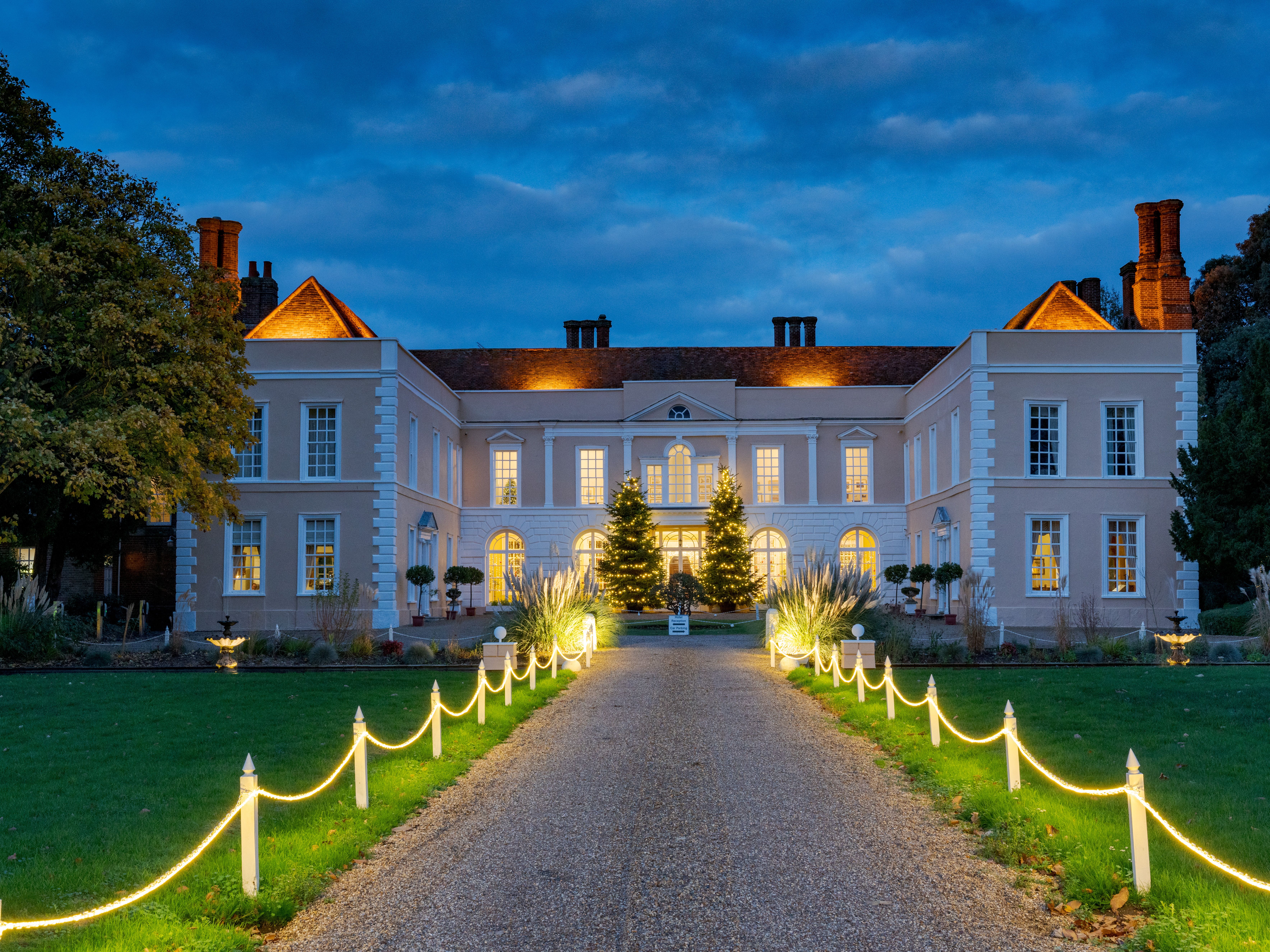 Illuminated country house at dusk with a lit pathway and Christmas trees in the entrance courtyard