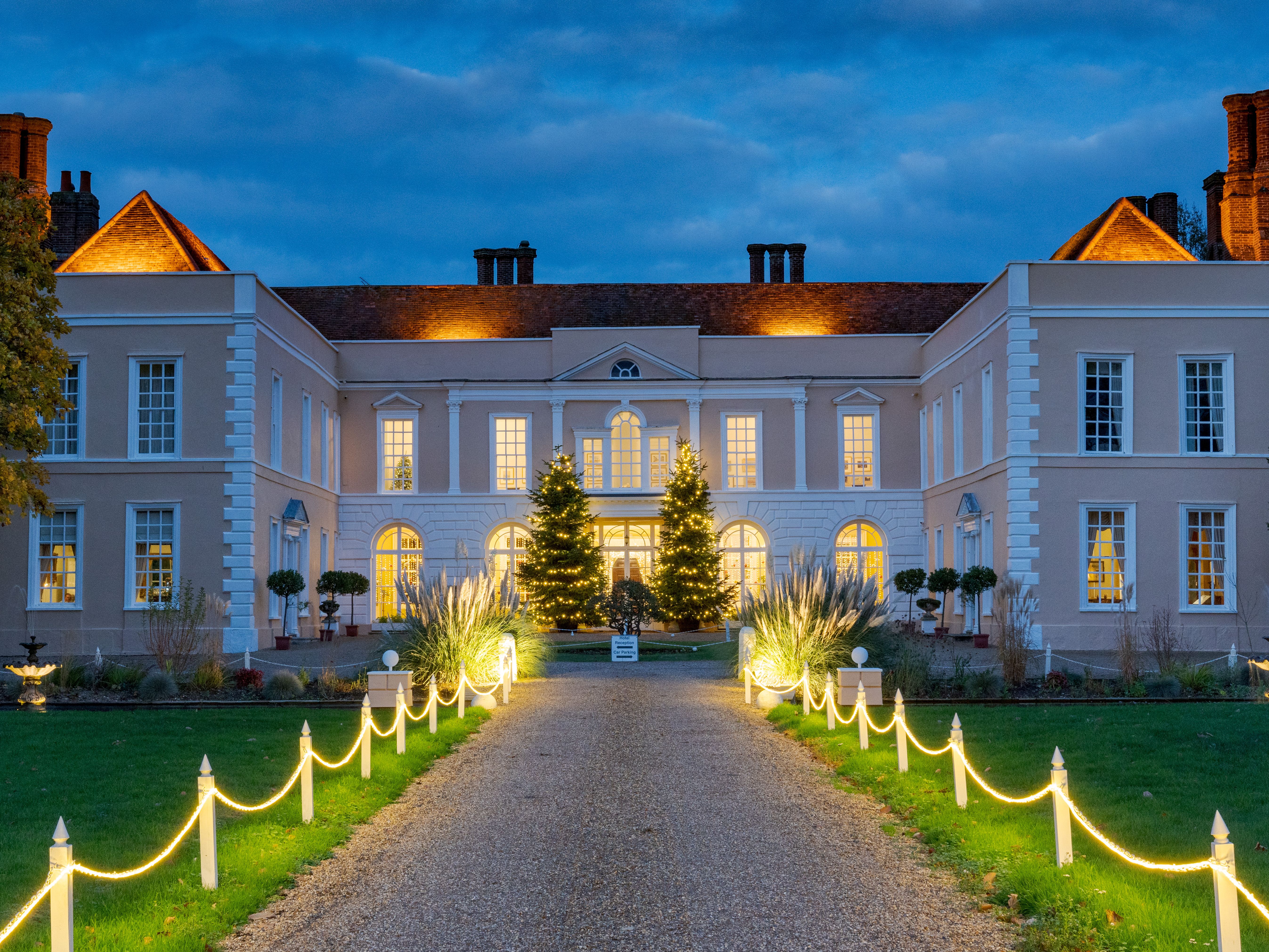 Illuminated country house at dusk with a lit pathway and Christmas trees in the entrance courtyard