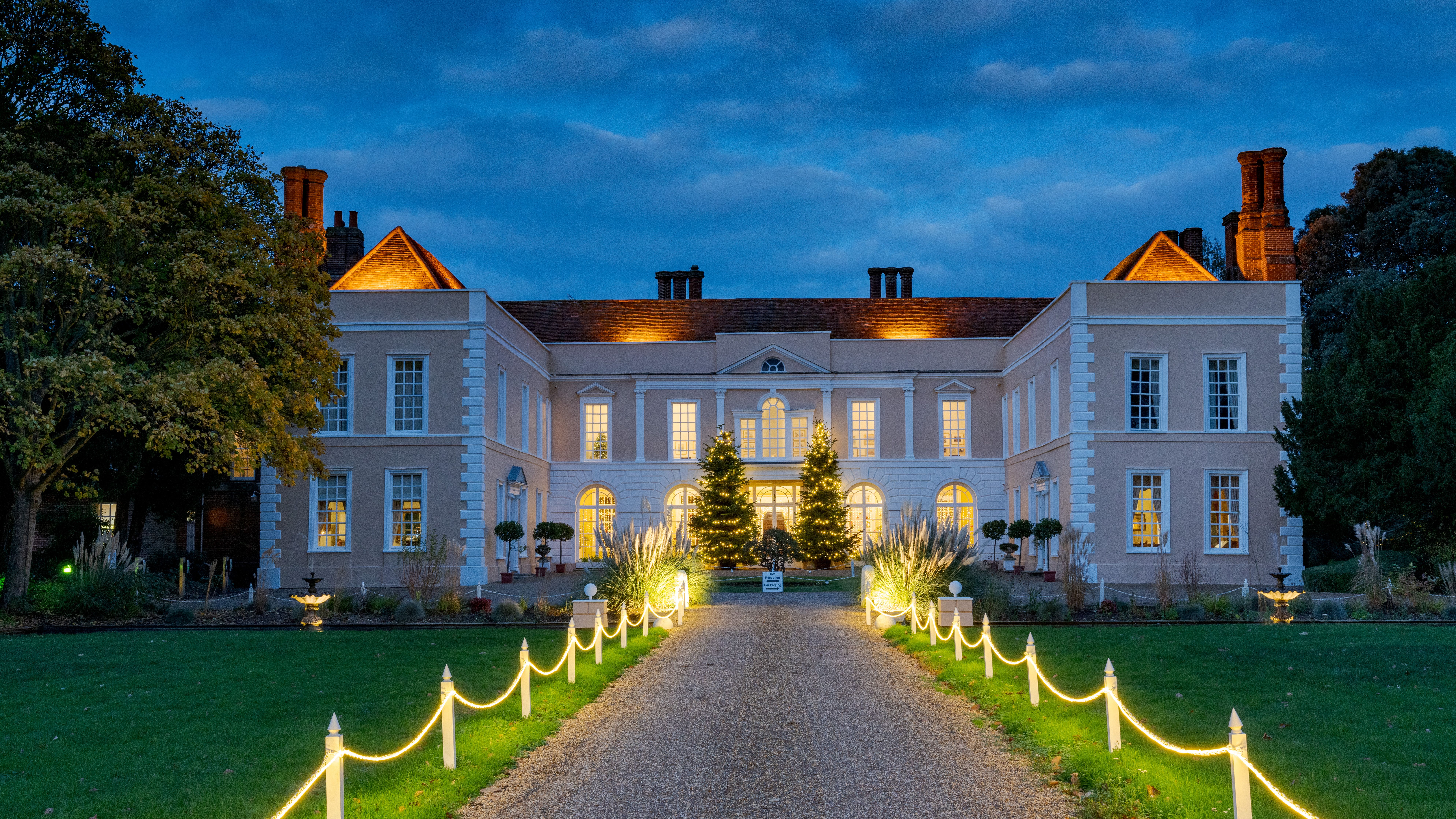 Illuminated country house at dusk with a lit pathway and Christmas trees in the entrance courtyard