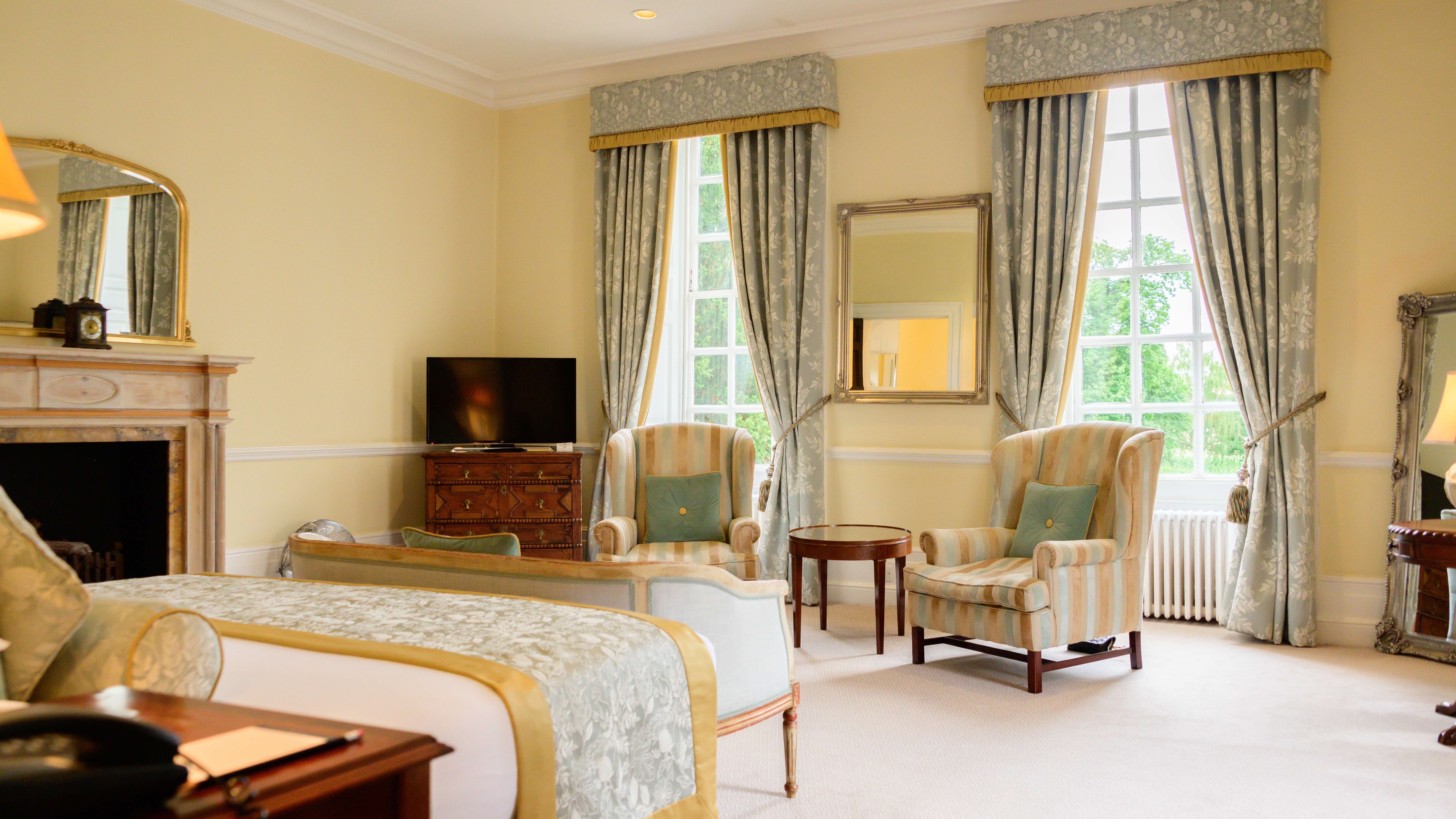 Elegant hotel room with armchairs, bed, fireplace, TV and large windows