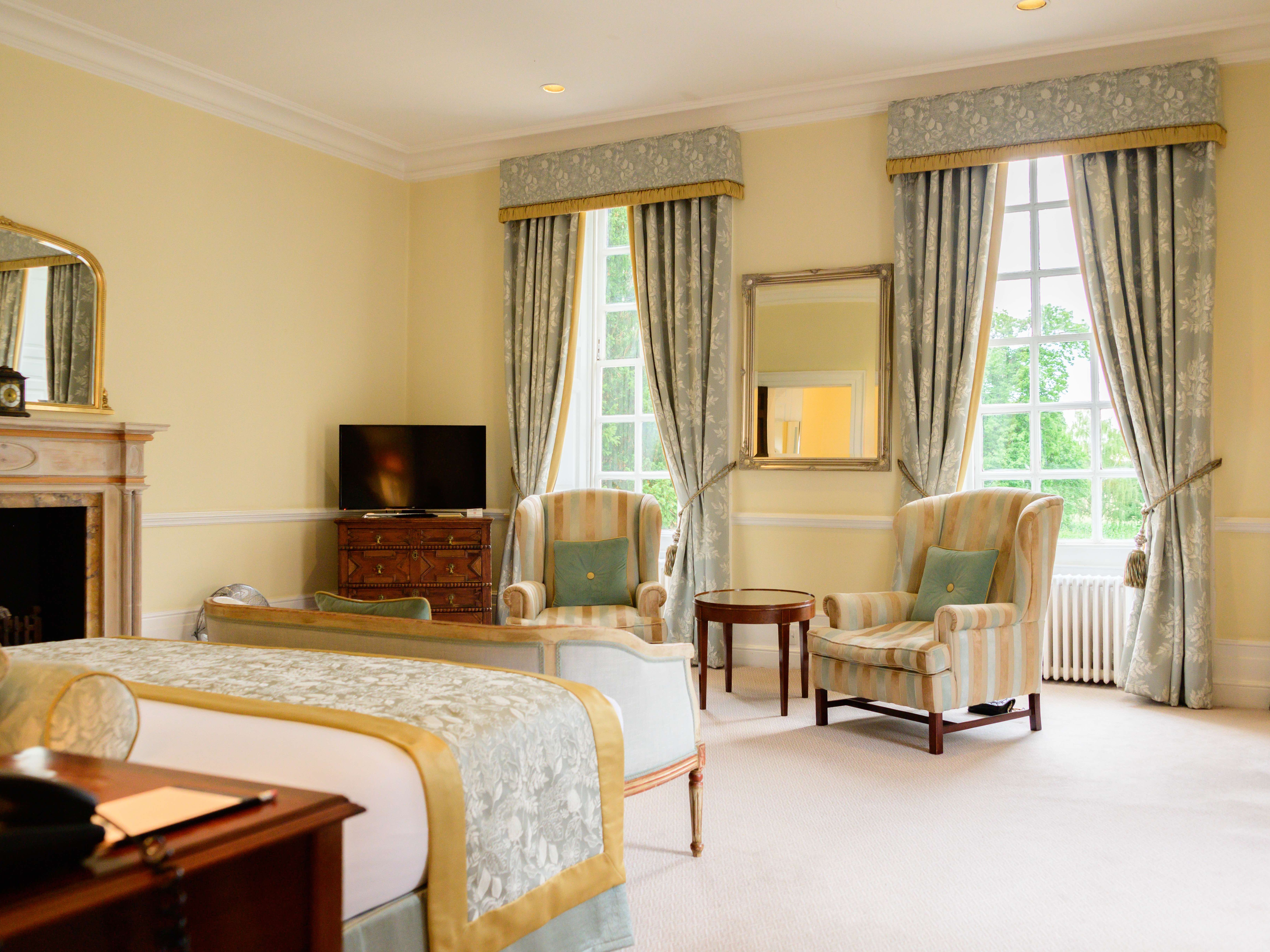 Elegant hotel room with armchairs, bed, fireplace, TV and large windows