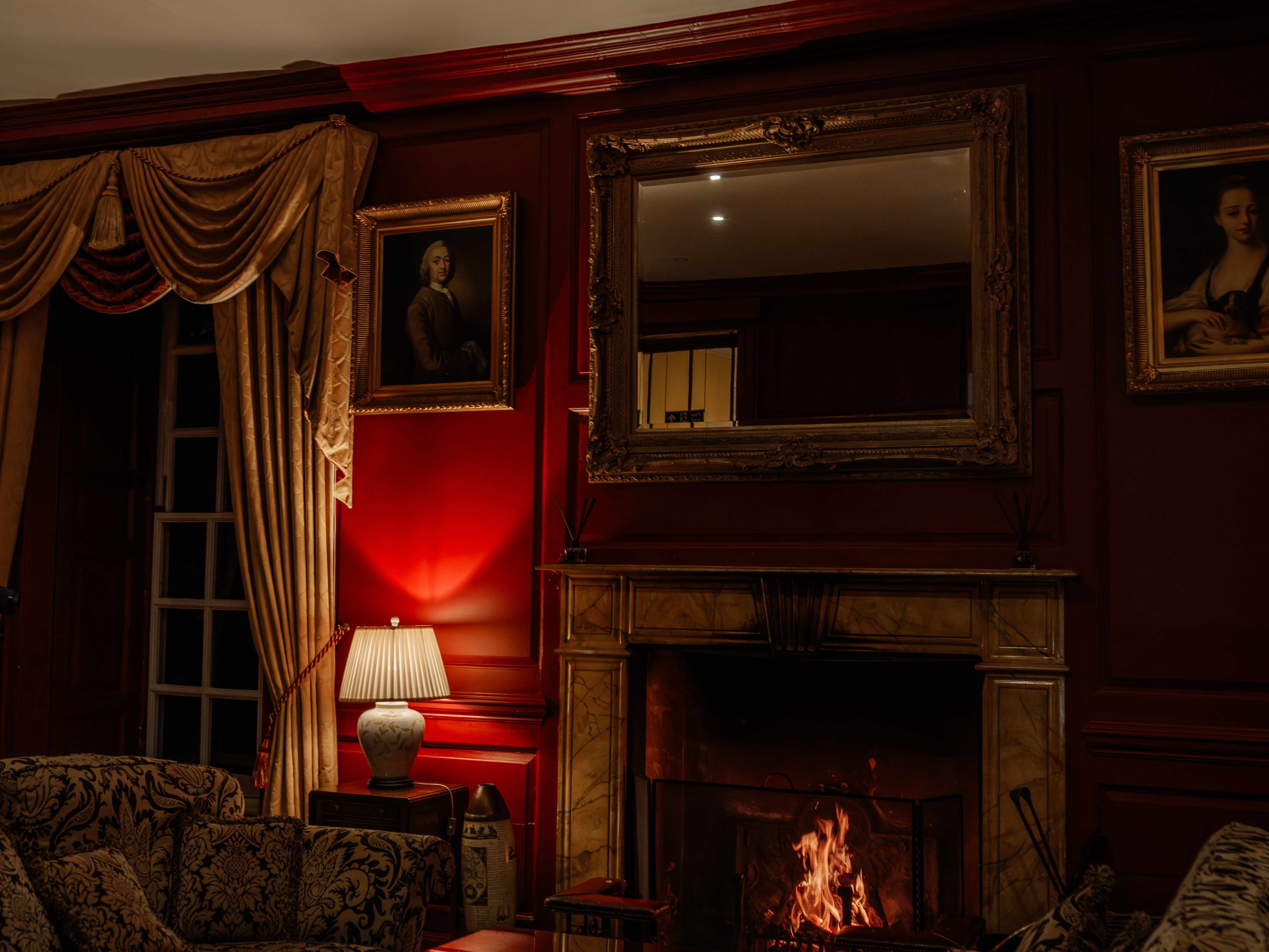Elegant living room with a lit fireplace, ornate furniture, red walls, and classic portraits.