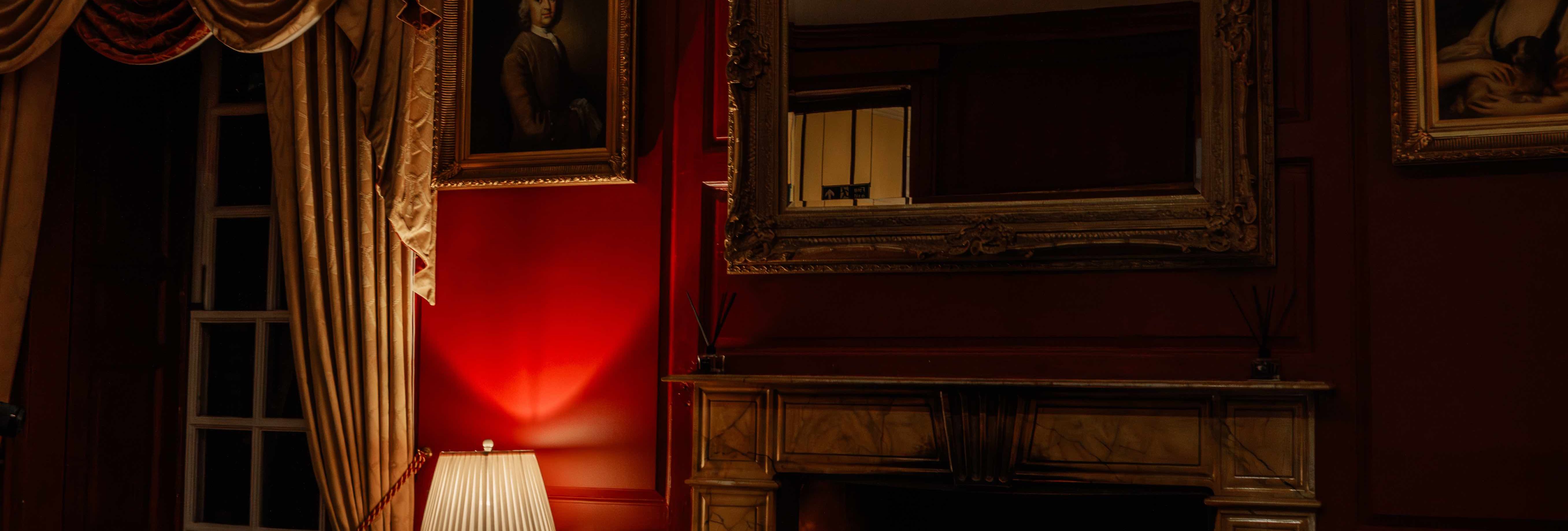 Elegant living room with a lit fireplace, ornate furniture, red walls, and classic portraits.