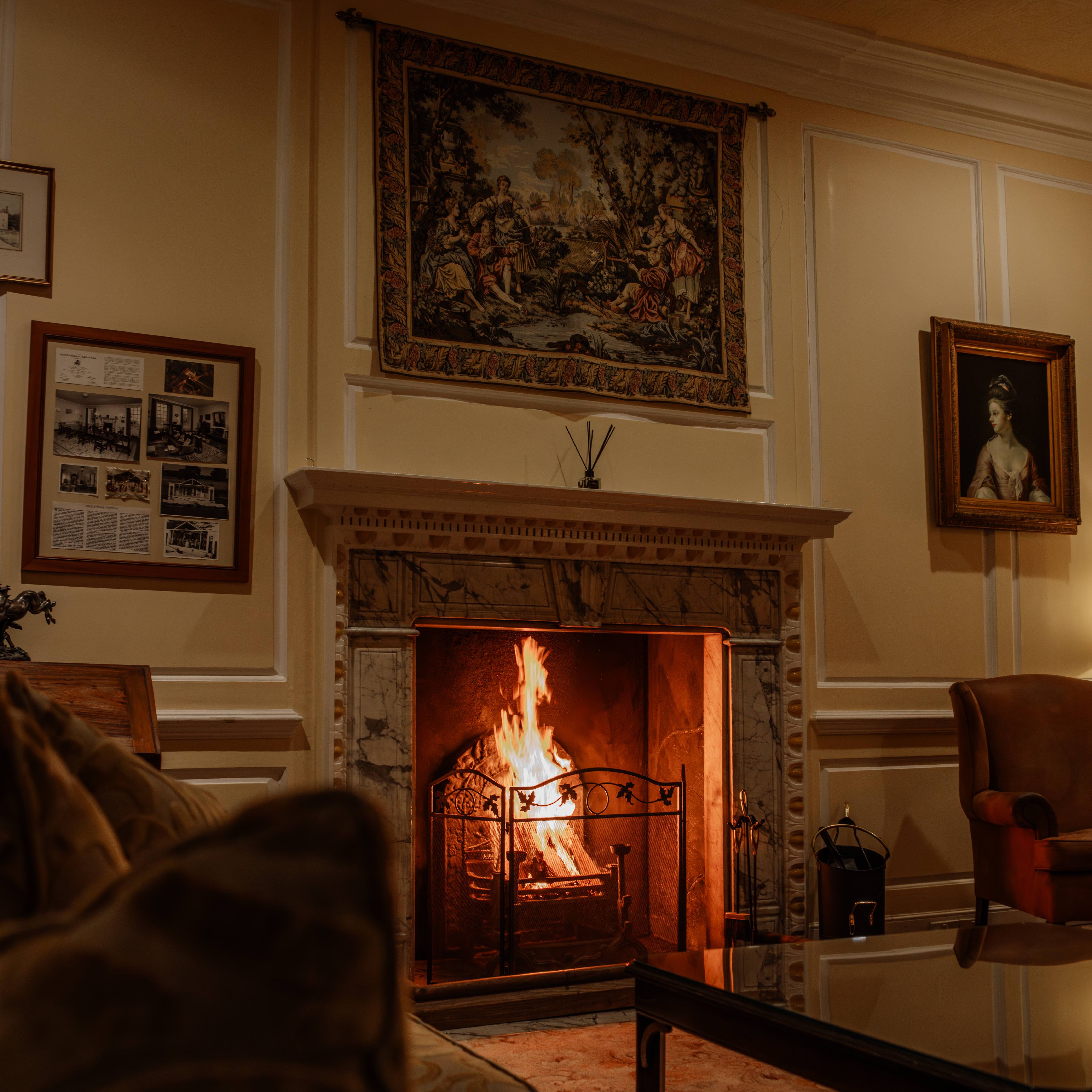 Cozy living room with a lit fireplace, ornate mantle, classic paintings, and comfortable seating.