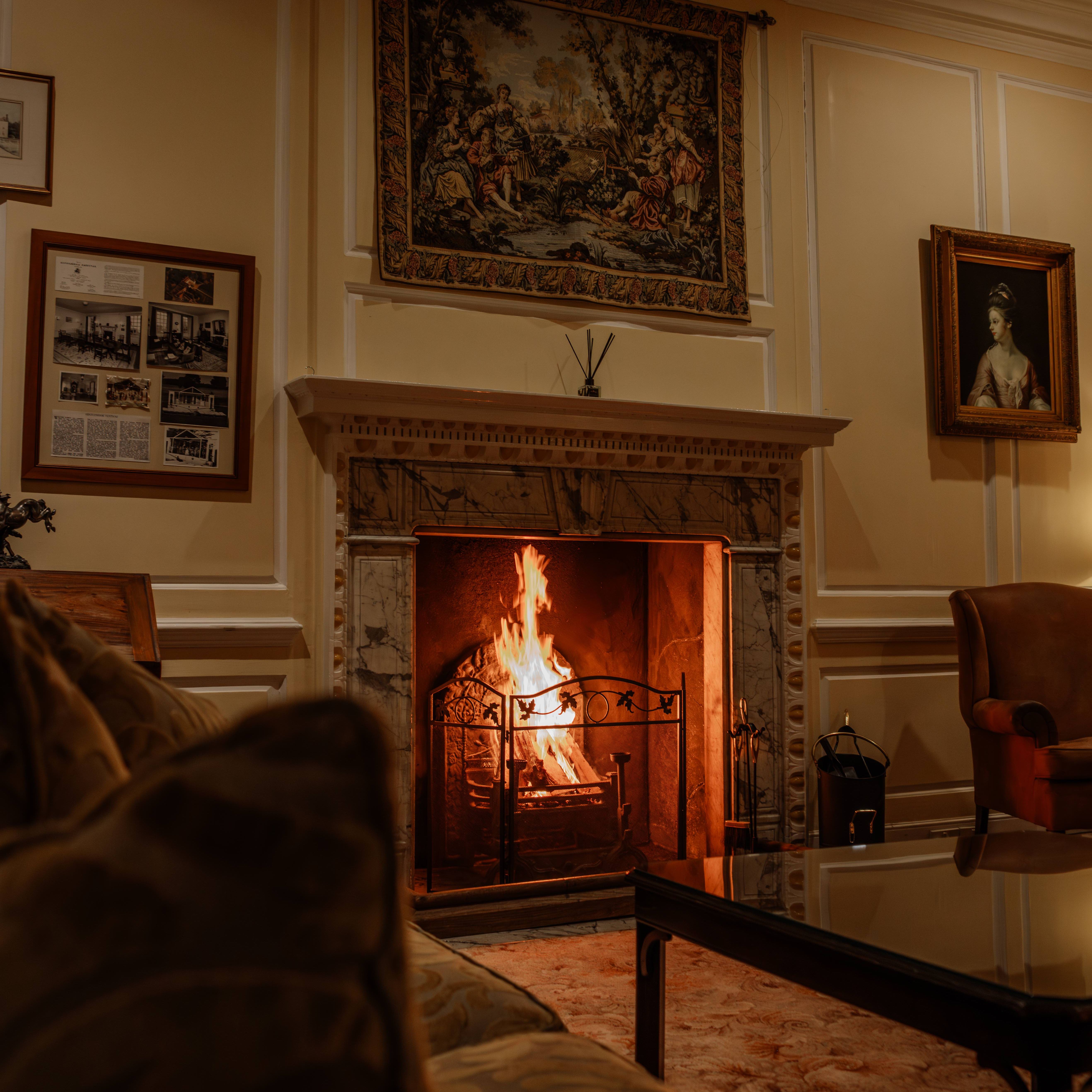 Cozy living room with a lit fireplace, ornate mantle, classic paintings, and comfortable seating.