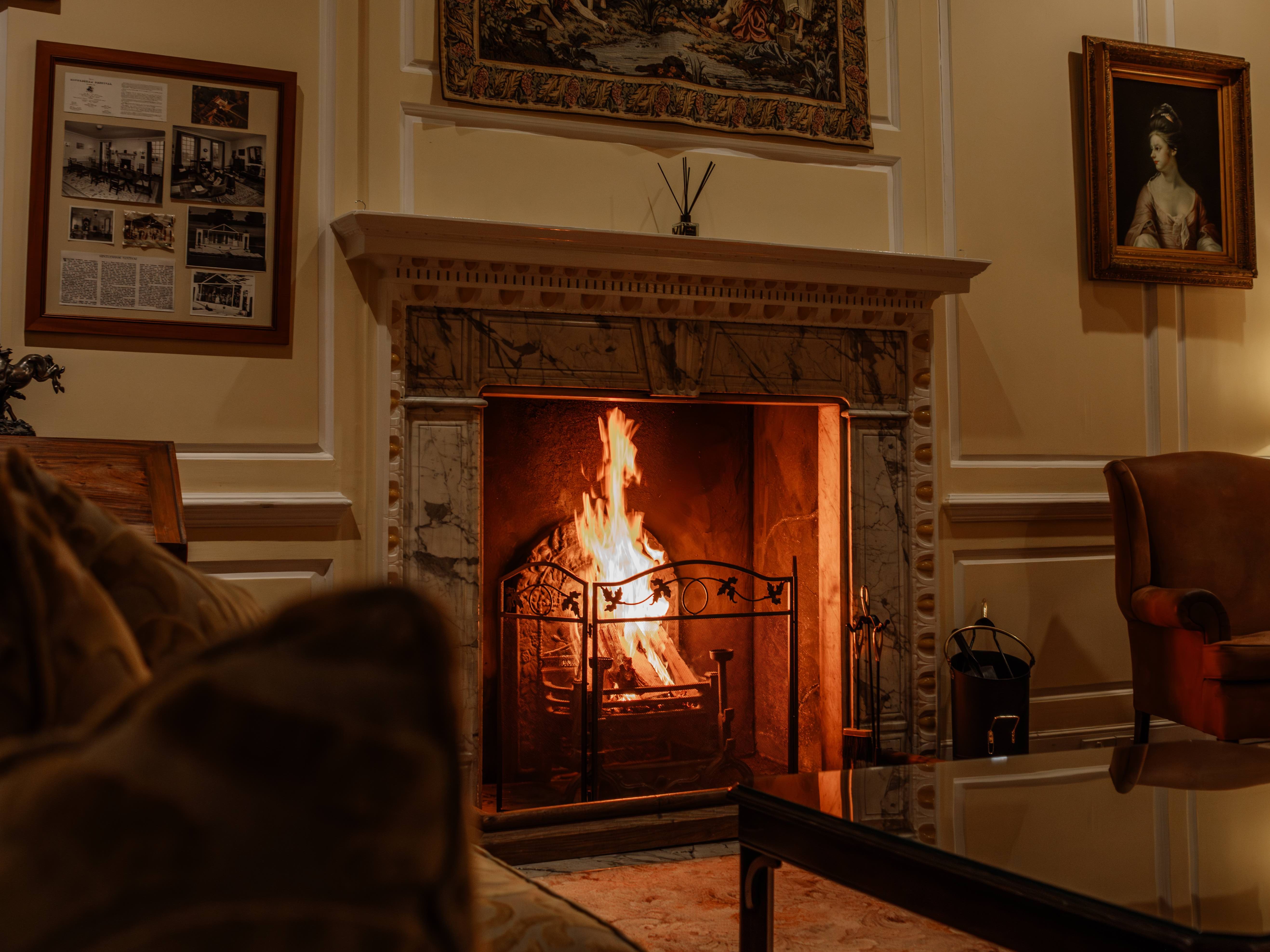 Cozy living room with a lit fireplace, ornate mantle, classic paintings, and comfortable seating.