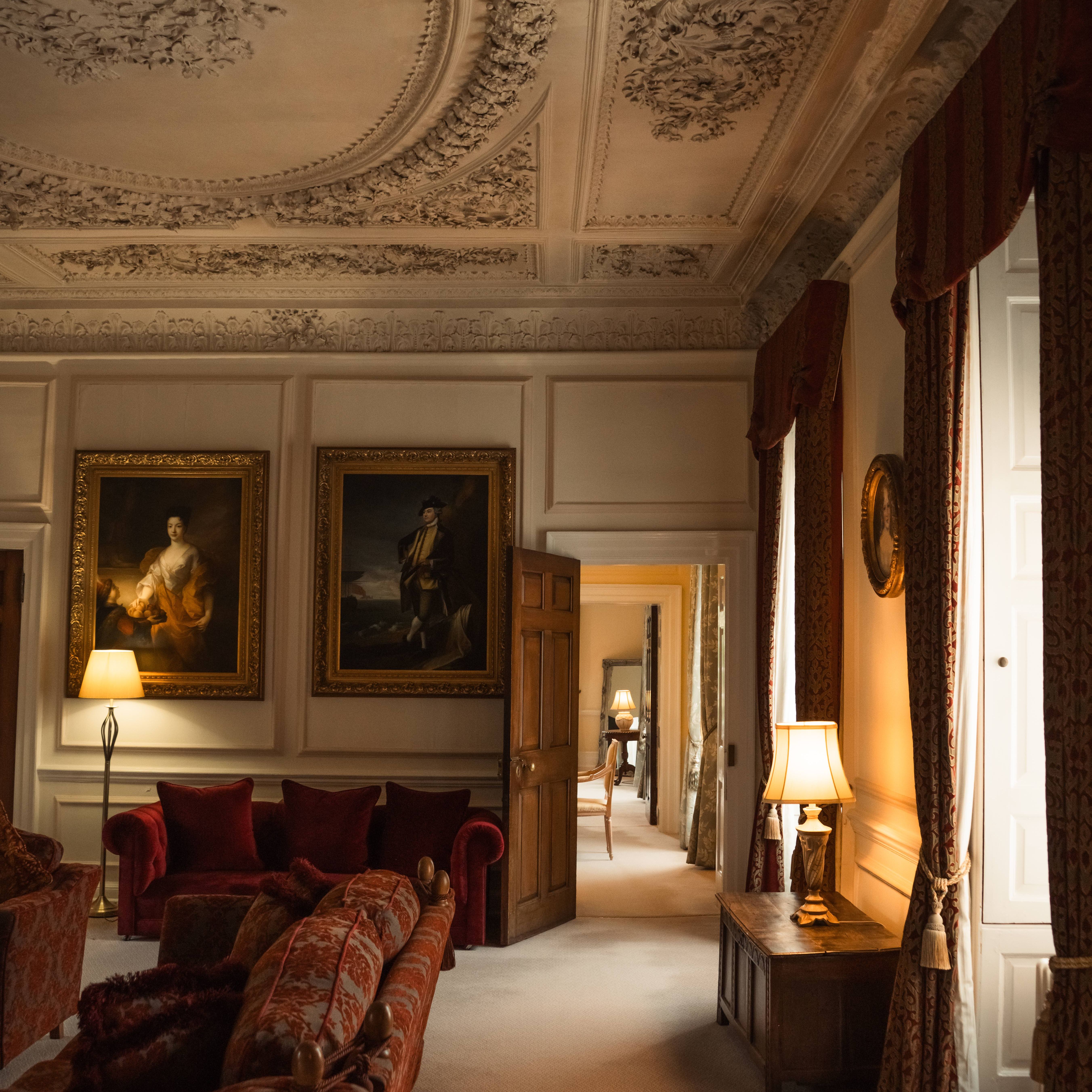Elegant historical living room with ornate ceiling, vintage furniture, and classical paintings.