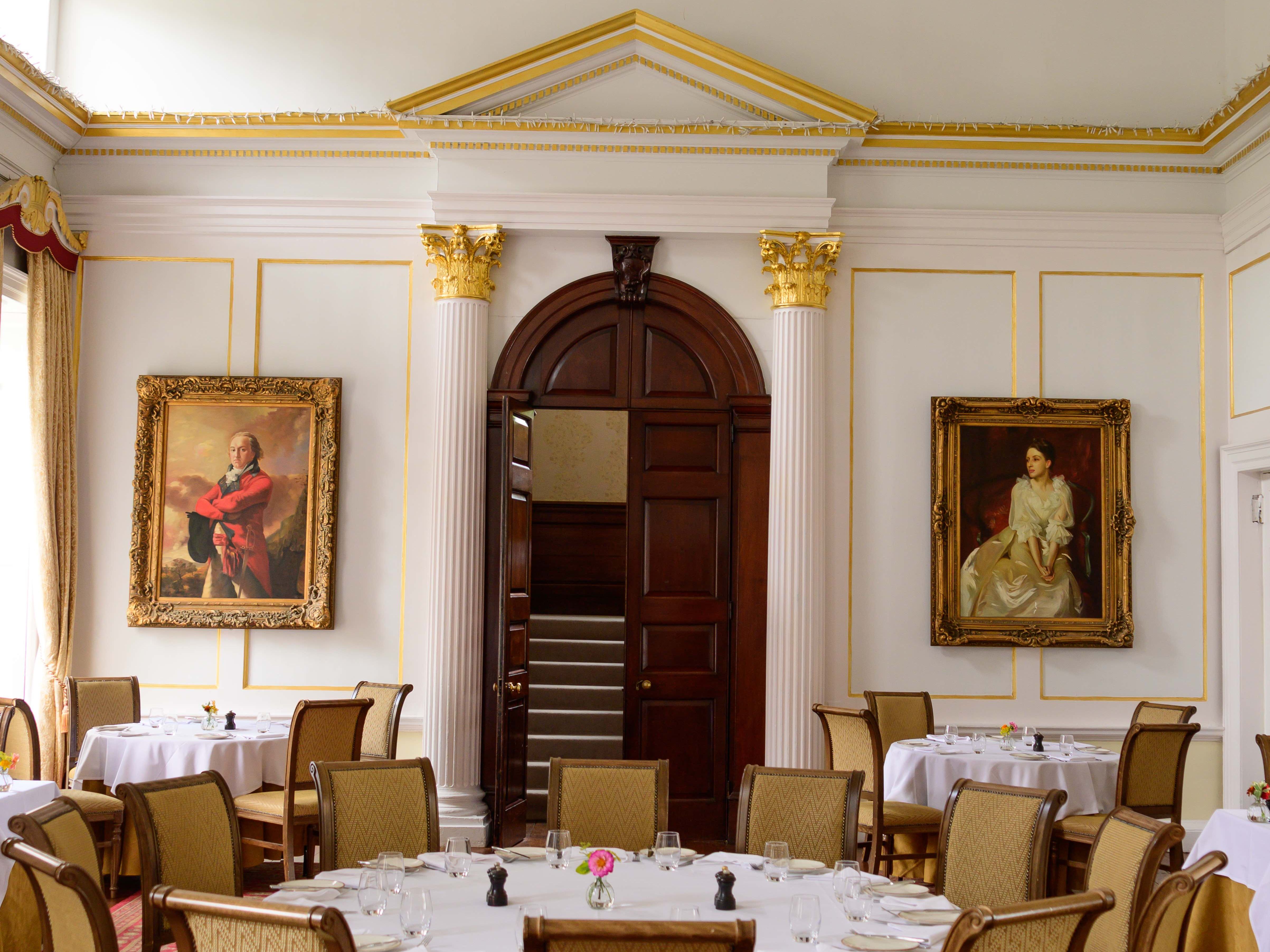 Elegant dining room with classic decor, round tables, a chandelier, and portrait paintings on the walls
