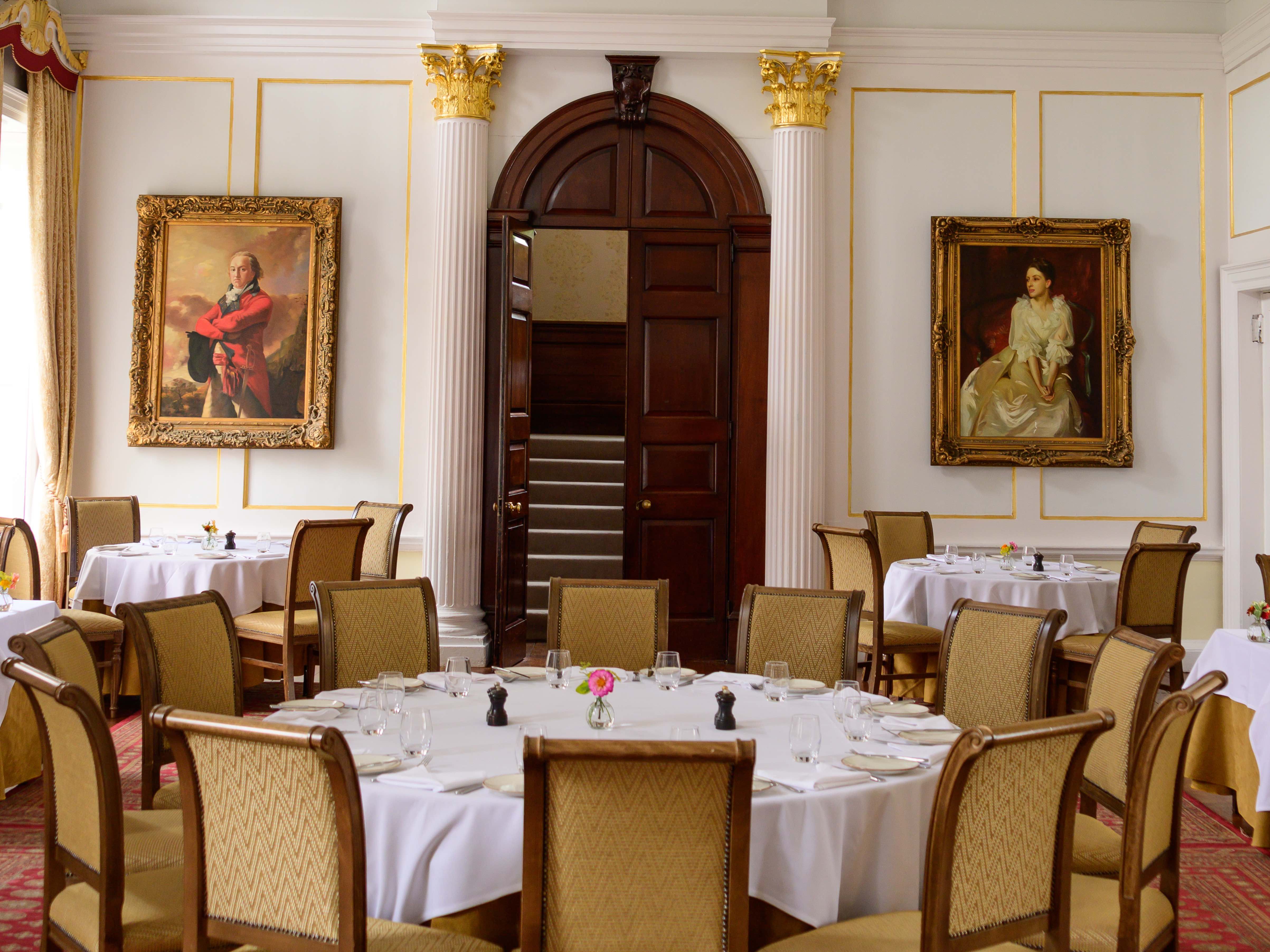 Elegant dining room with classic decor, round tables, a chandelier, and portrait paintings on the walls