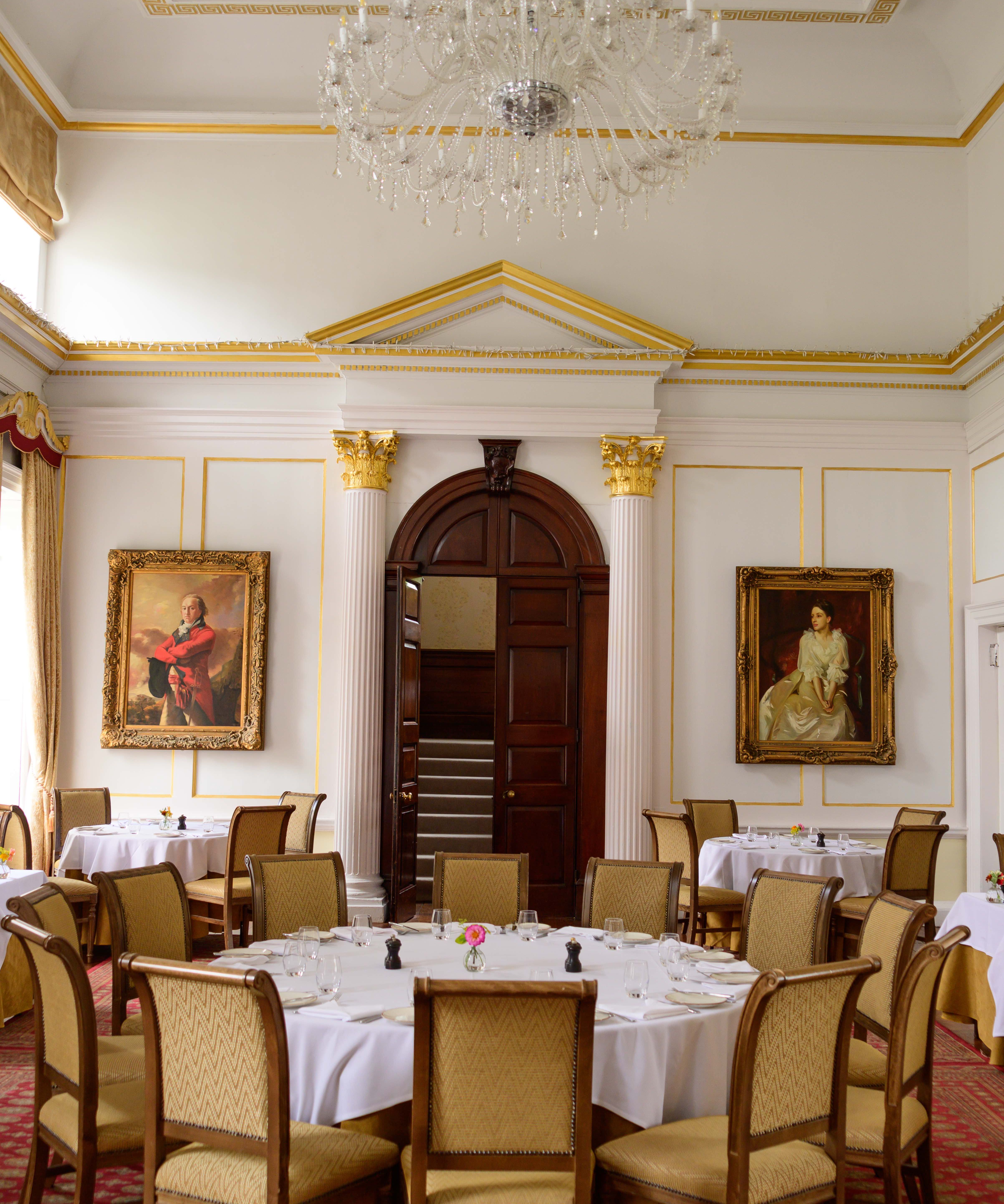 Elegant dining room with classic decor, round tables, a chandelier, and portrait paintings on the walls