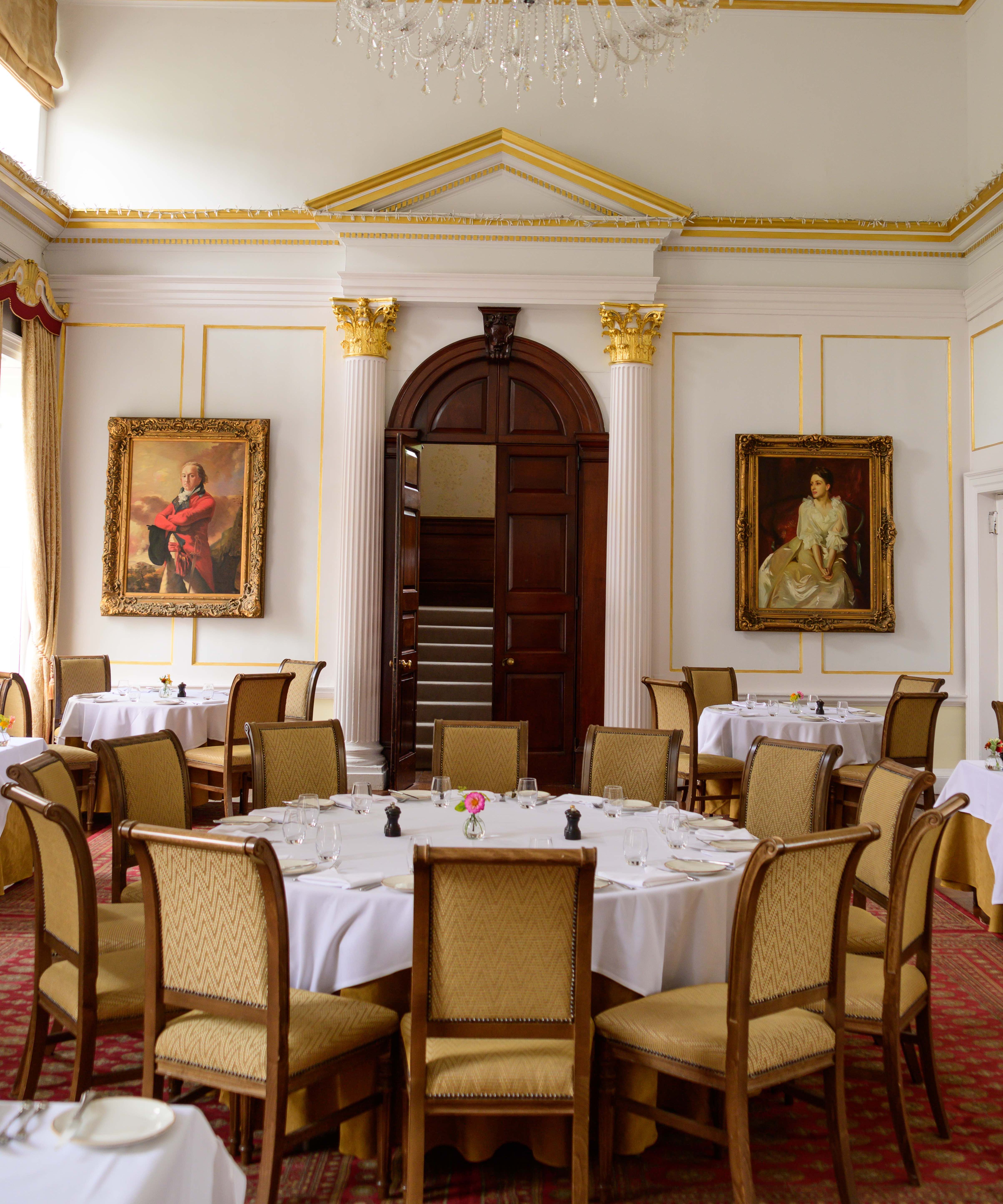 Elegant dining room with classic decor, round tables, a chandelier, and portrait paintings on the walls
