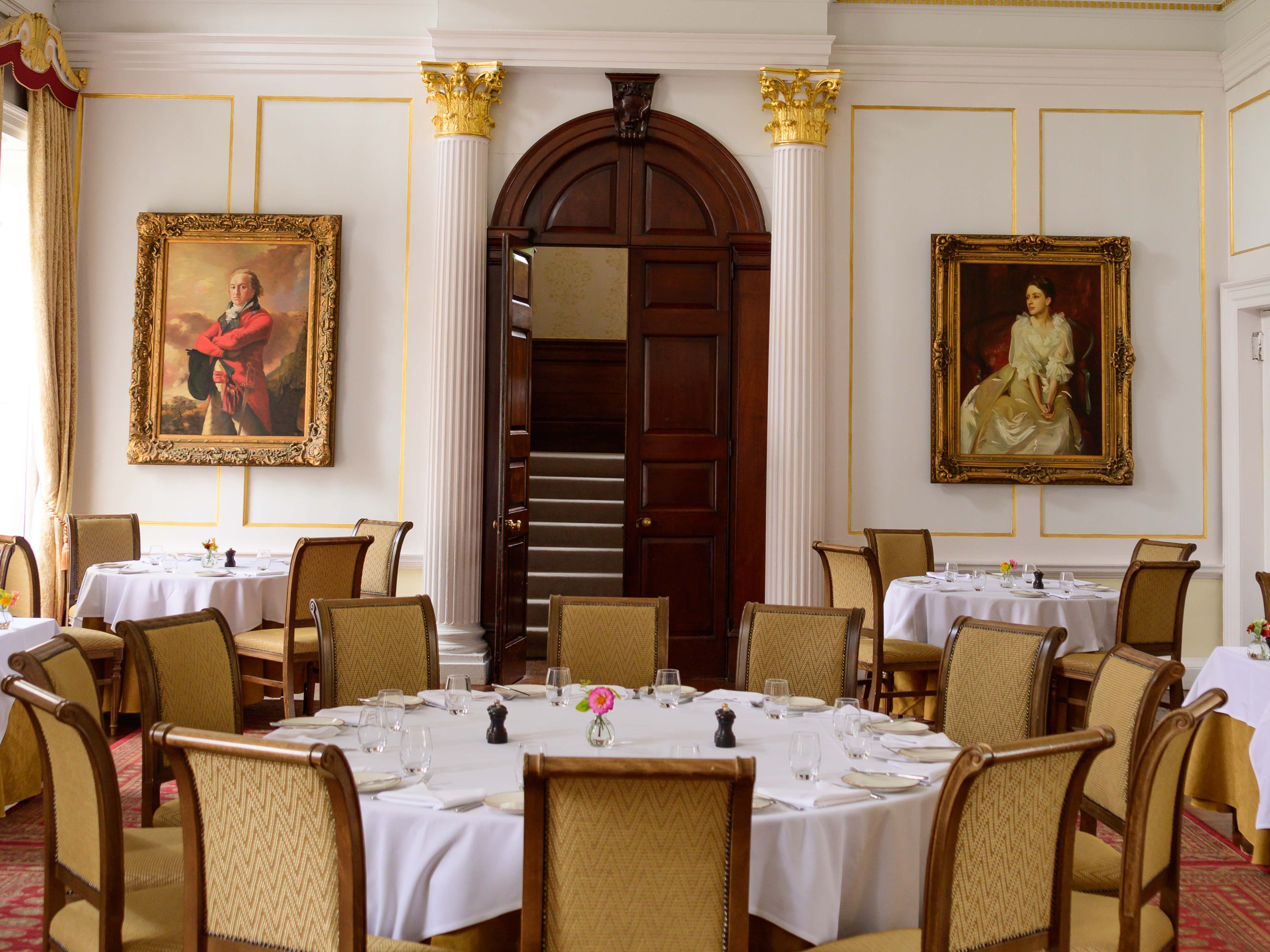 Elegant dining room with classic decor, round tables, a chandelier, and portrait paintings on the walls