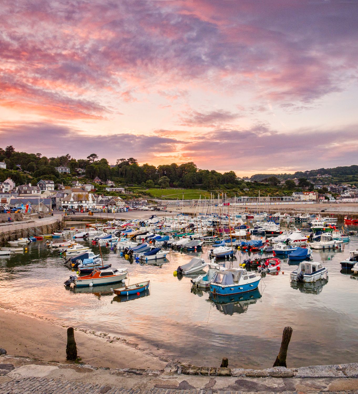 The historic harbour at Lyme Regis, Dorset, England, on a summer evening, with the Cobb and boats under a red sunset sky.