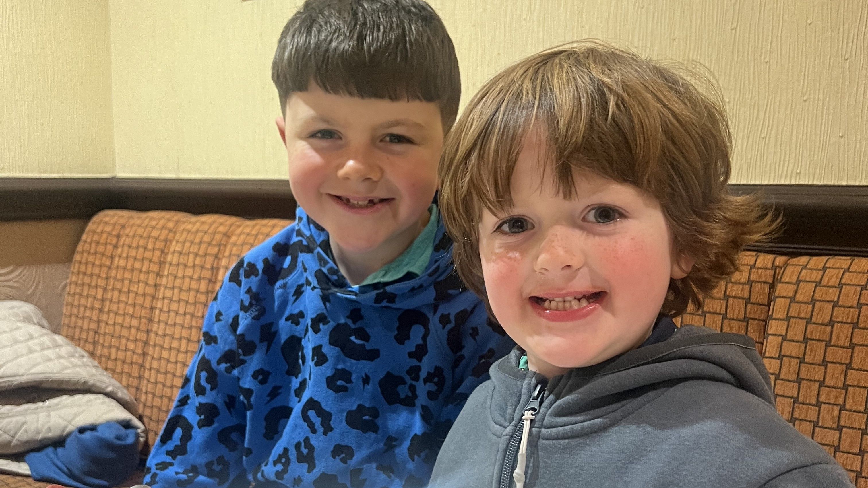 Two young children smiling and sitting together at a restaurant table