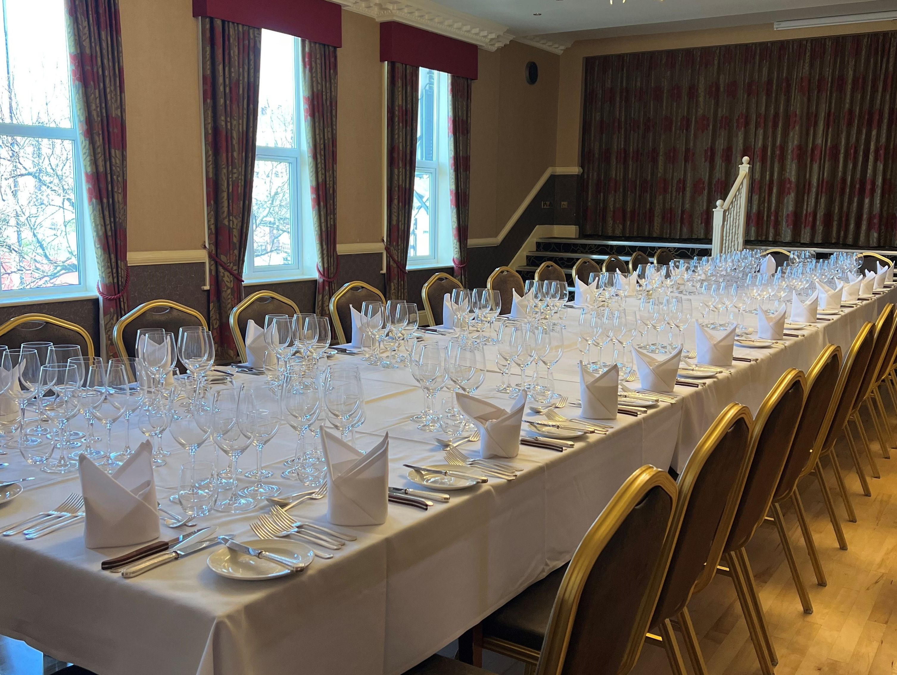 Formal dining room with long tables set with white linens, glassware, cutlery, and folded napkins.