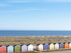 Row of colorful beach huts by the seaside with sand dunes and calm blue sea under a clear sky