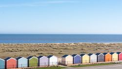 Row of colorful beach huts by the seaside with sand dunes and calm blue sea under a clear sky