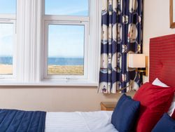 Coastal hotel room with nautical-themed curtains, red and blue pillows, and a sea view through the window