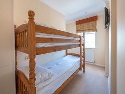 Wooden bunk beds in a small, well-lit hotel room with cream-colored walls and a window with a plaid blind