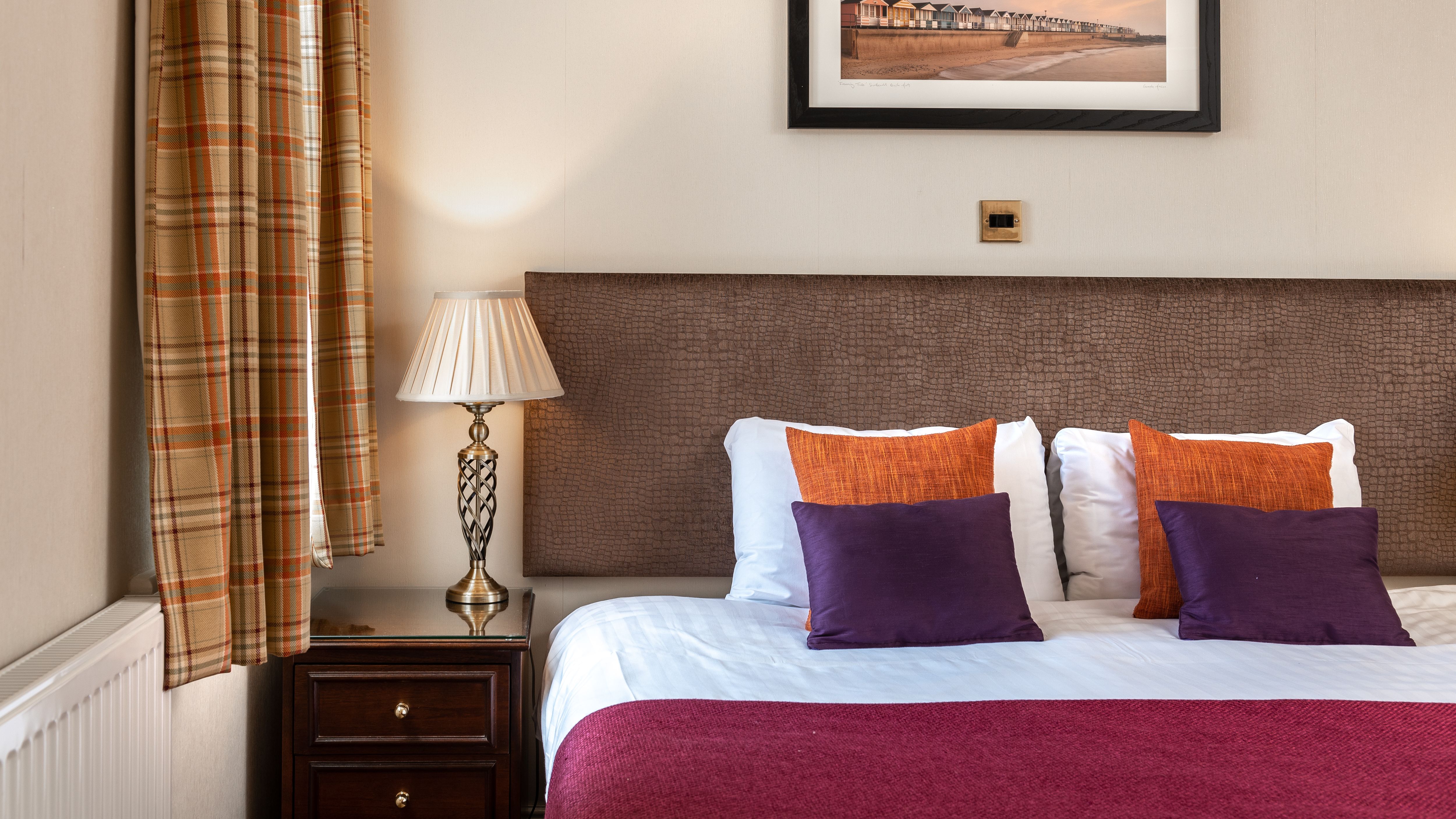 Elegant hotel room with double bed, decorative pillows, side table with lamp, and framed artwork above the headboard