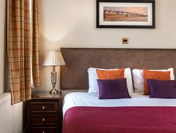 Elegant hotel room with double bed, decorative pillows, side table with lamp, and framed artwork above the headboard