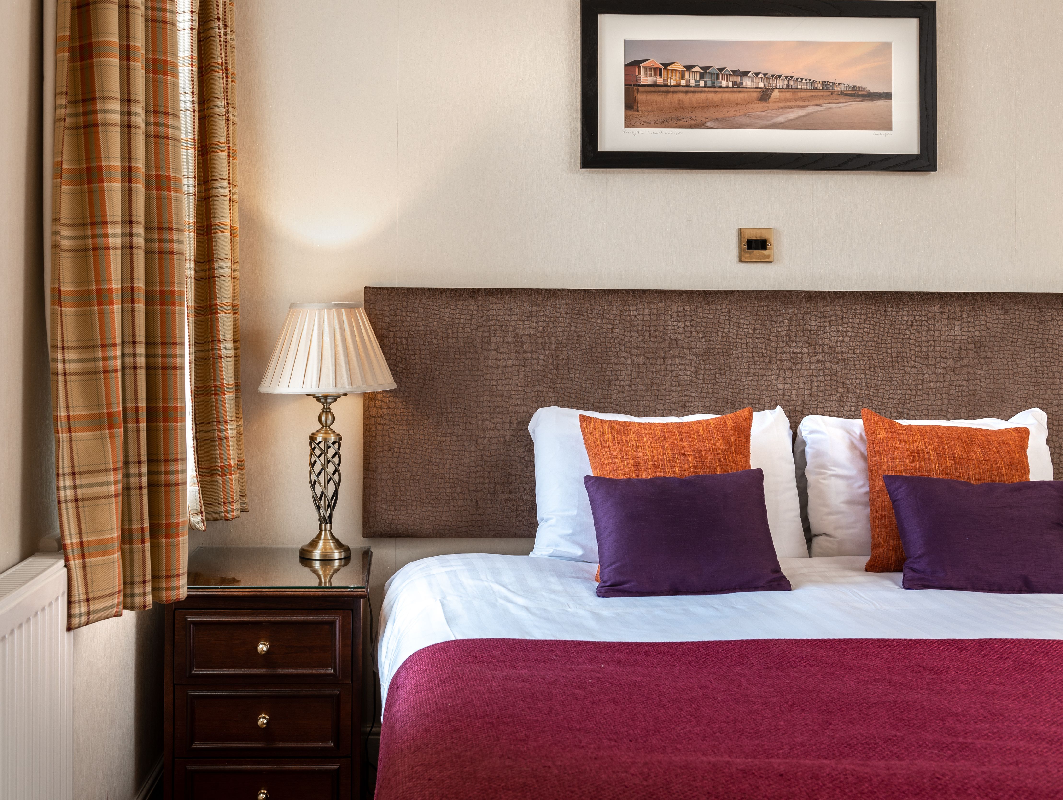Elegant hotel room with double bed, decorative pillows, side table with lamp, and framed artwork above the headboard