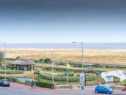 Seaside park with pavilion, gardens, and distant wind turbines along the coast