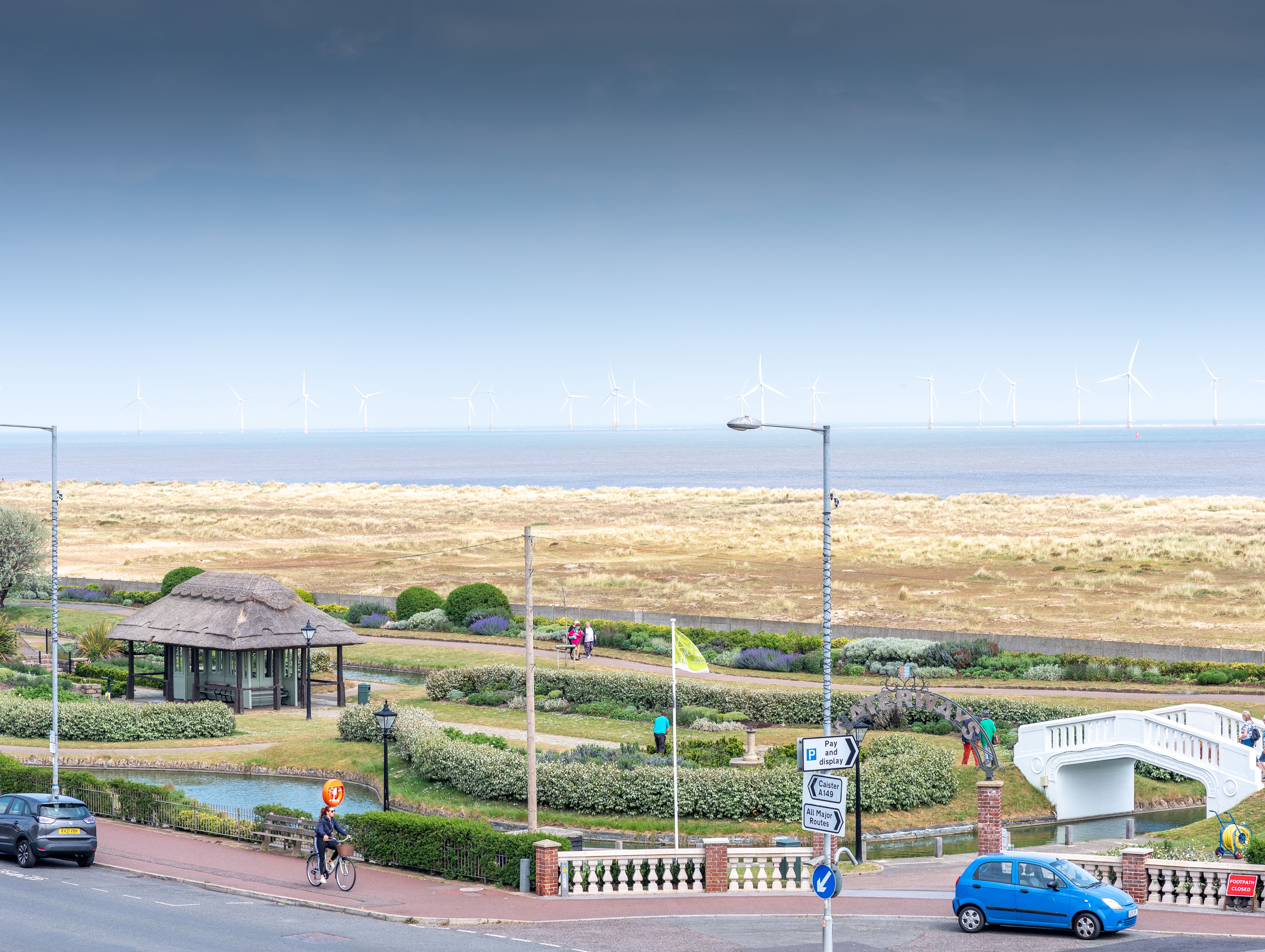 Seaside park with pavilion, gardens, and distant wind turbines along the coast