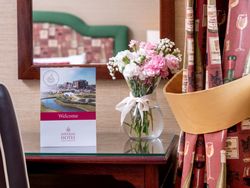 Elegant hotel bedroom detail with a vase of pink and white flowers, welcome card, and decorative curtains.