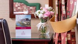 Elegant hotel bedroom detail with a vase of pink and white flowers, welcome card, and decorative curtains.