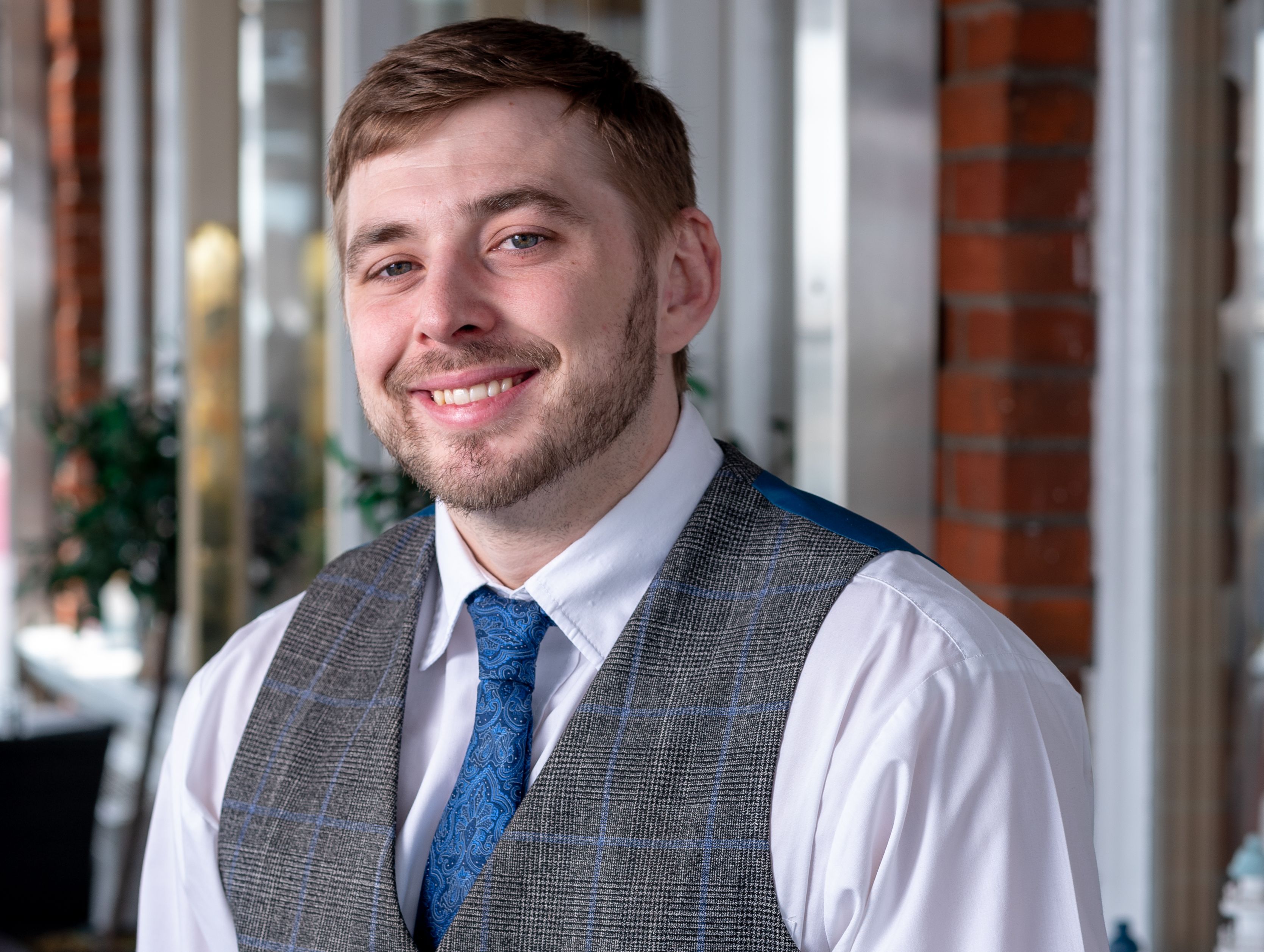 Smiling hotel staff member in a vest and tie standing indoors