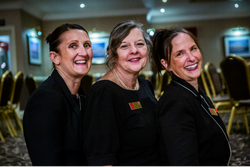 Three women smiling and posing together in a conference or meeting room.