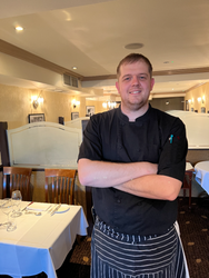 Chef standing with arms crossed in a restaurant dining area