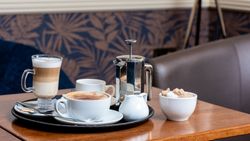Tray with cappuccino, latte, French press, and sugar bowl on a coffee shop table