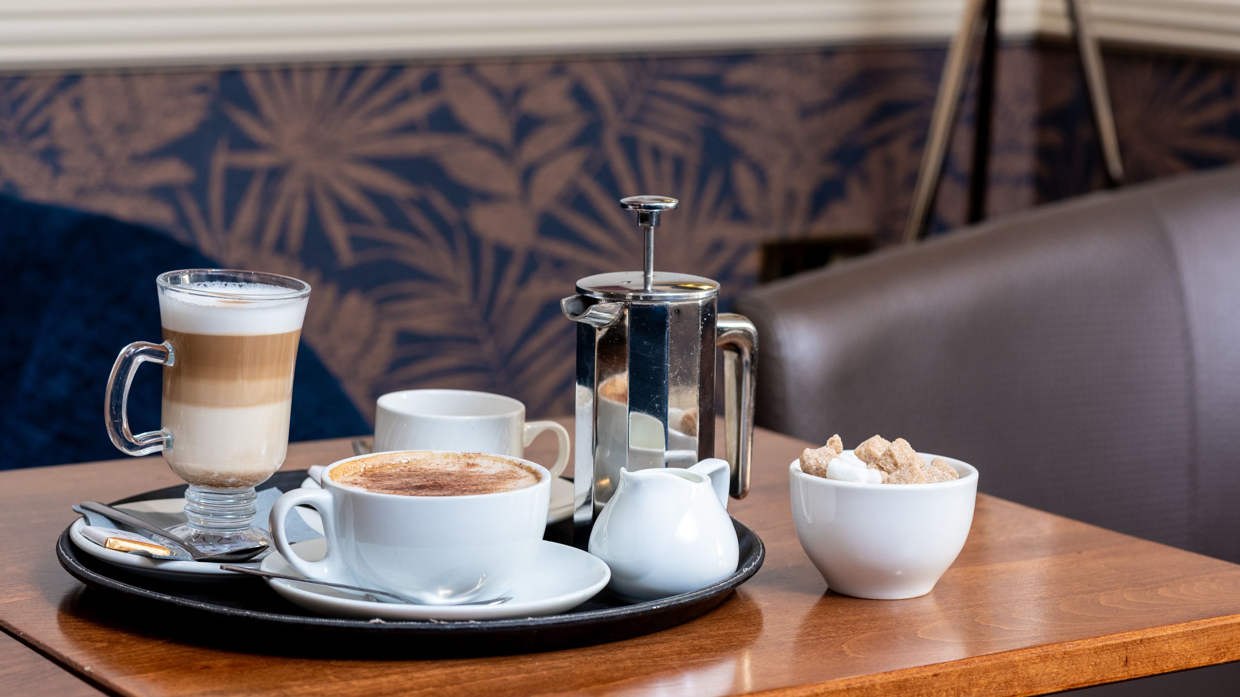 Tray with cappuccino, latte, French press, and sugar bowl on a coffee shop table