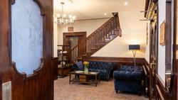 Elegant hotel lobby with dark blue sofas, wooden staircase, glass coffee table with flowers, and chandelier lighting.