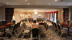 Conference room set up with rows of chairs and tables, featuring a chandelier and large windows with curtains.